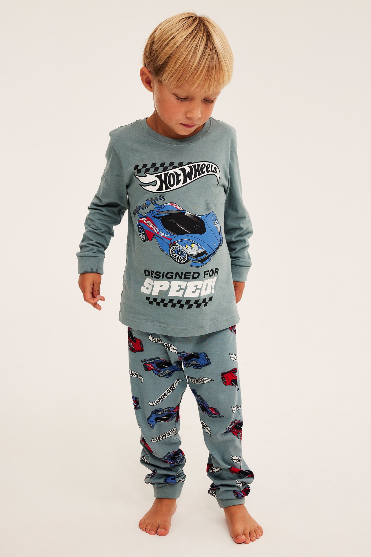 Edestä: lapsi käyttää sinistä Hot Wheels -pyjamasettiä autokuvioinnilla.