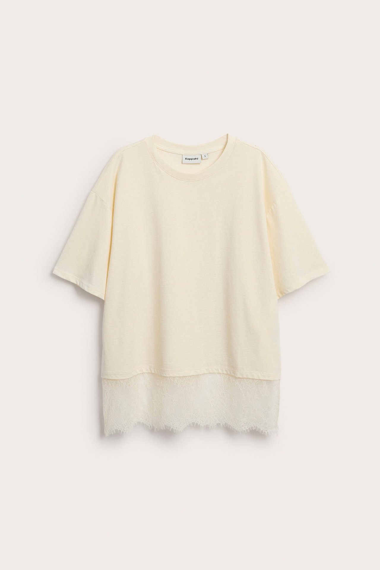 Frontbilde av en oversized kremfarget t-skjorte med hvit blondekant.