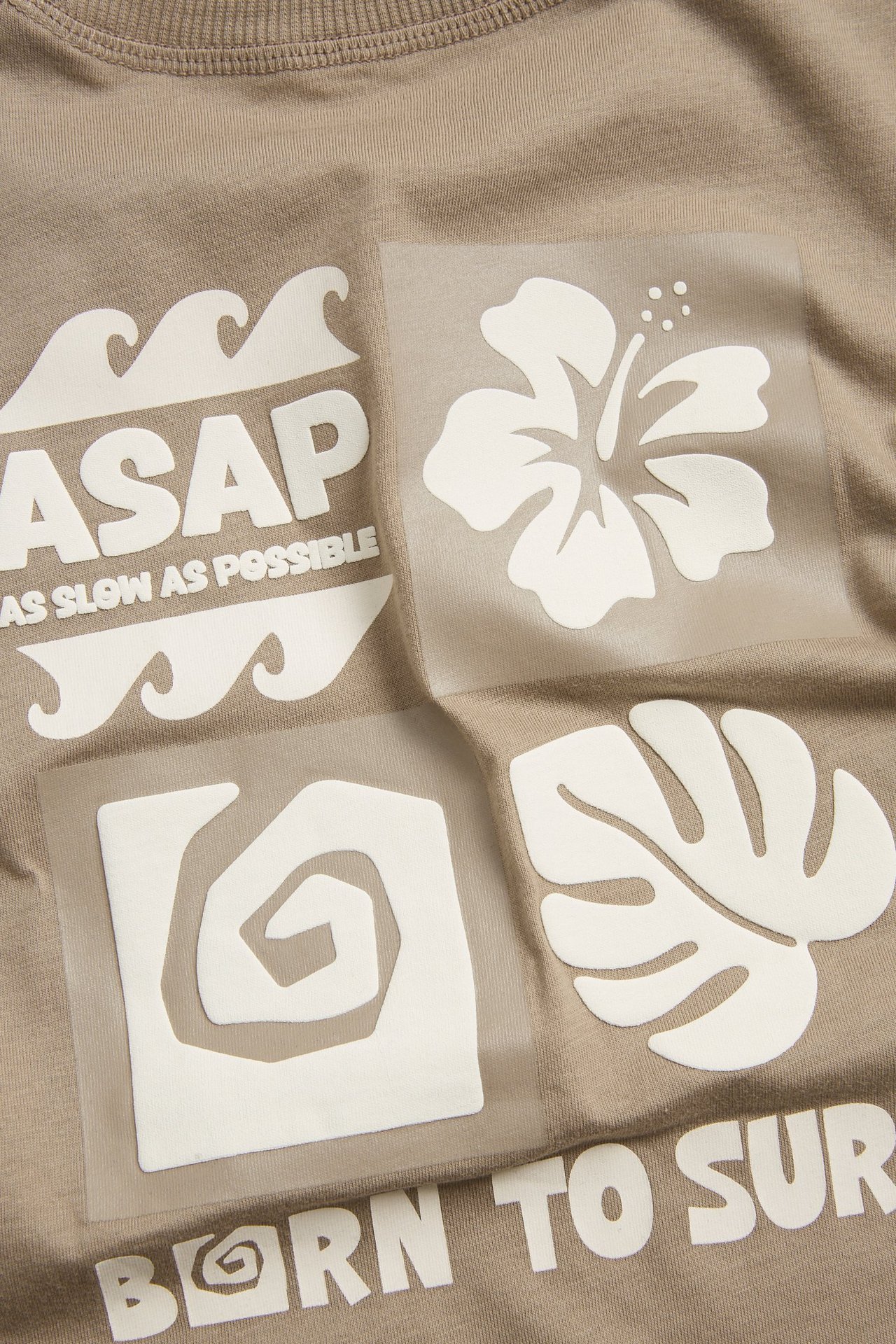 Zbliżenie: brązowy bawełniany T-shirt oversize z dużym białawym nadrukiem i tropikalnymi motywami.