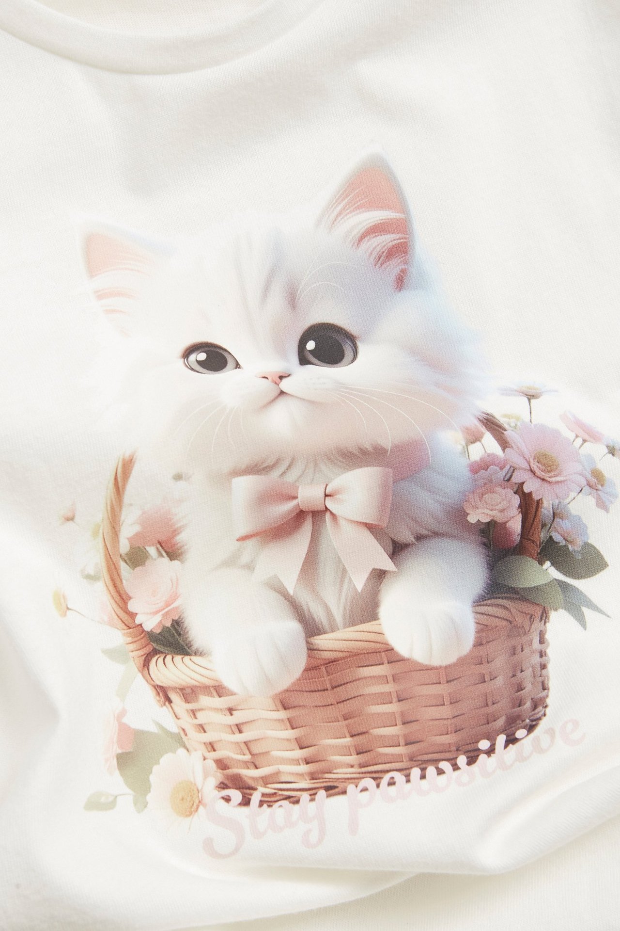 Widok z przodu na ecru bawełniany T-shirt dziecięcy z dużym nadrukiem kotka w koszyku z kwiatami.