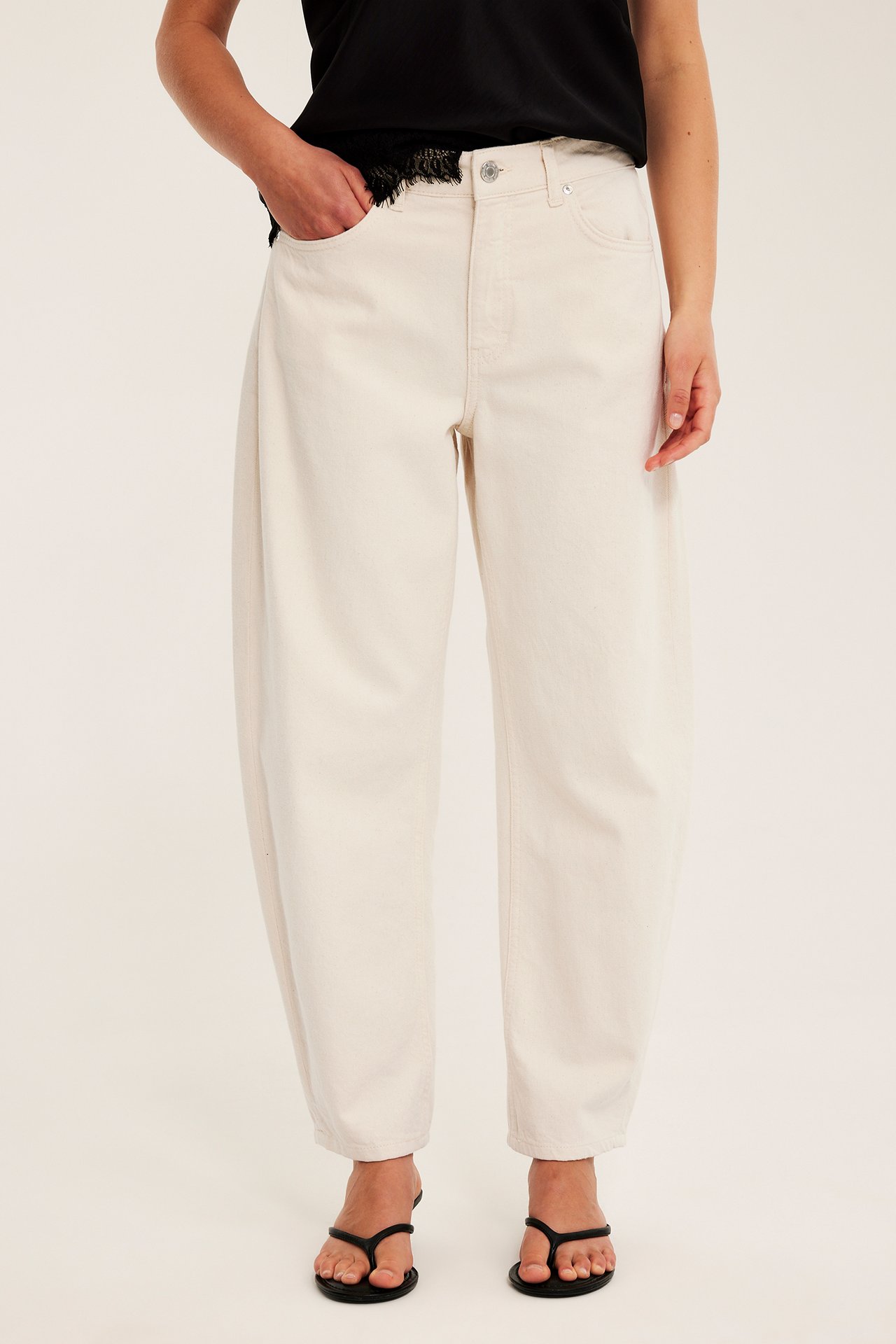 Naisen etunäkymä: valkoiset korkeavyötäröiset barrel-farkut, musta toppi ja mustat varvassandaalit.