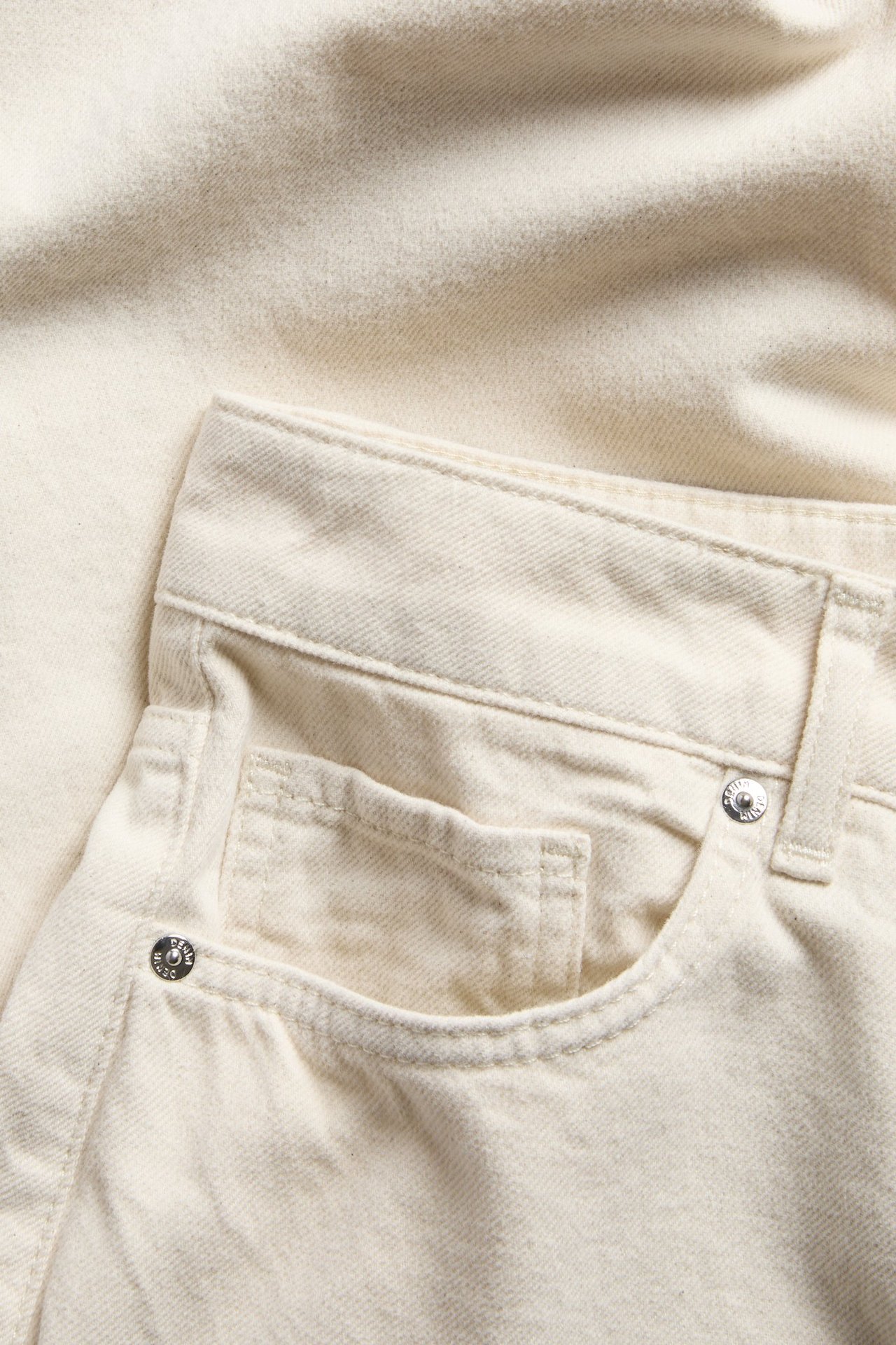 Lähikuva valkoisista puuvillaisista korkeavyötäröisistä barrel-farkuista, joissa on etutasku ja hopeanapit.