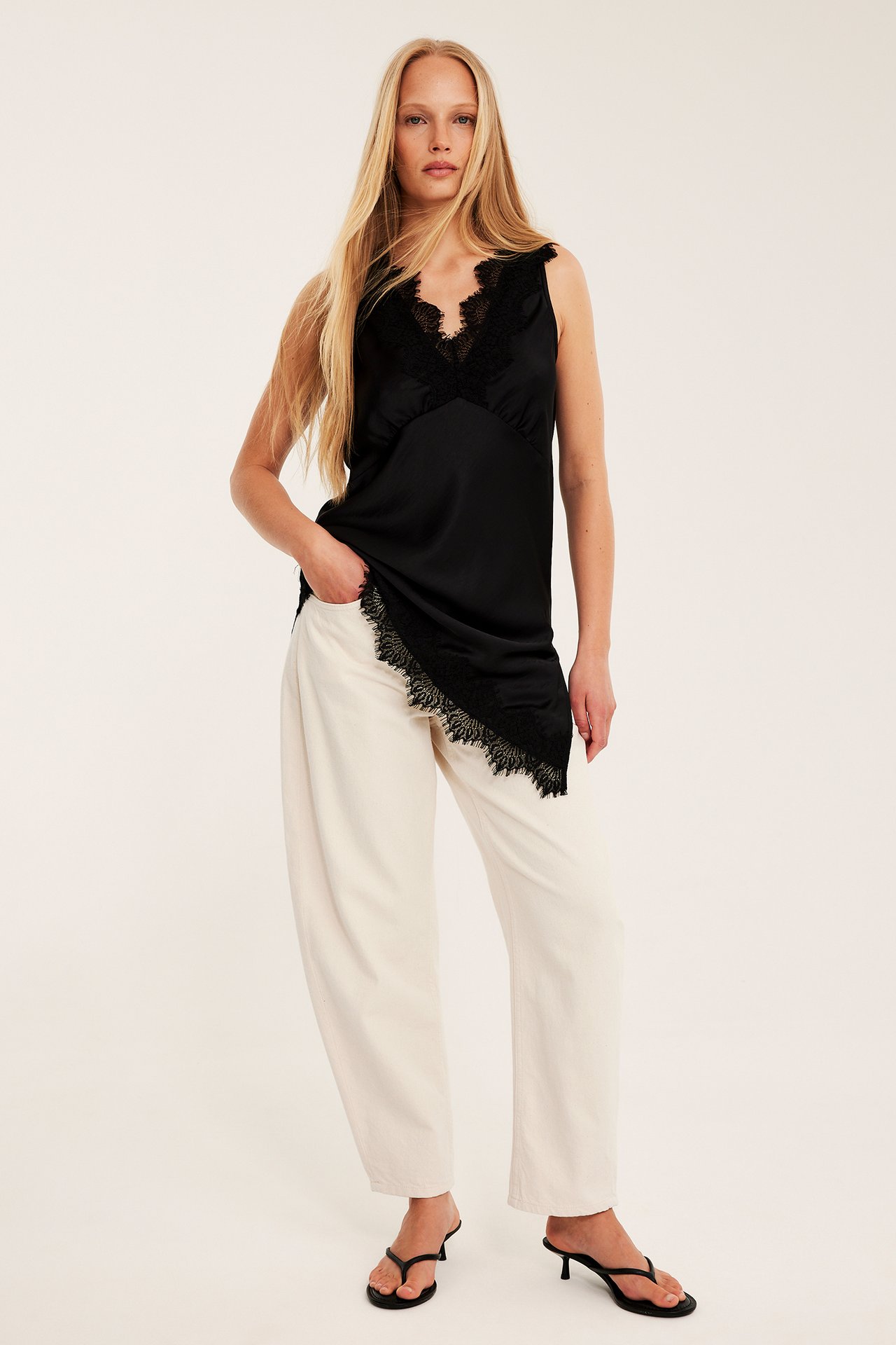 Etunäkymä: nainen valkoisissa barrel-farkuissa, musta pitsitoppi ja mustat korkosandaalit.