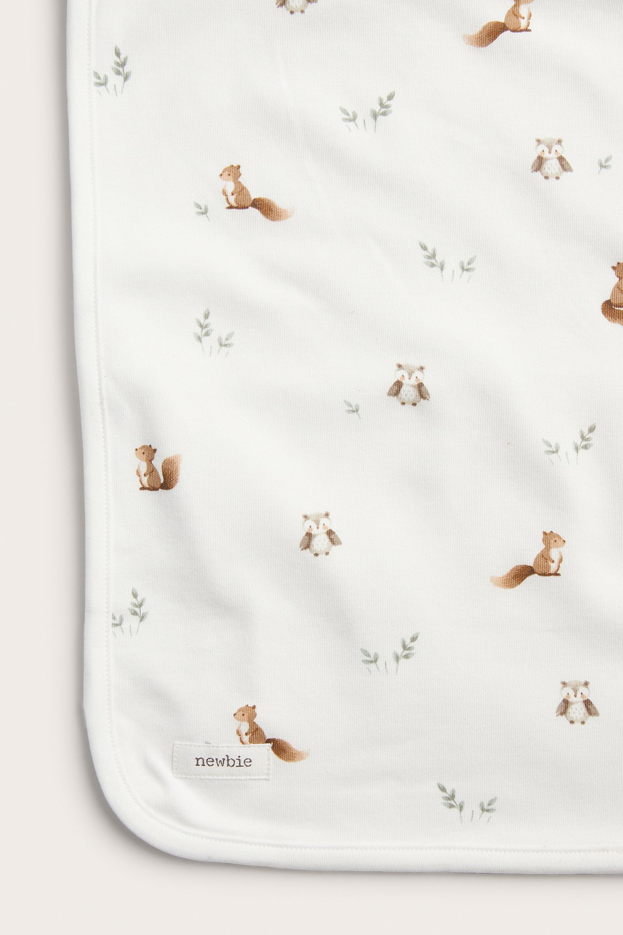 Lähikuva valkoisesta vauvanpeitosta, jossa ruskea orava- ja pöllökuvio.