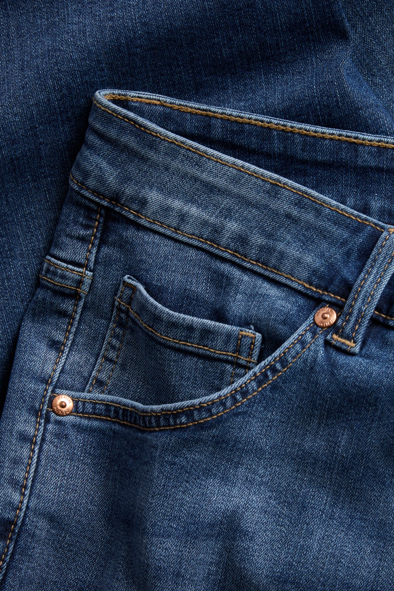 Närbild på blå denimjeans med kopparnitar på framfickan.