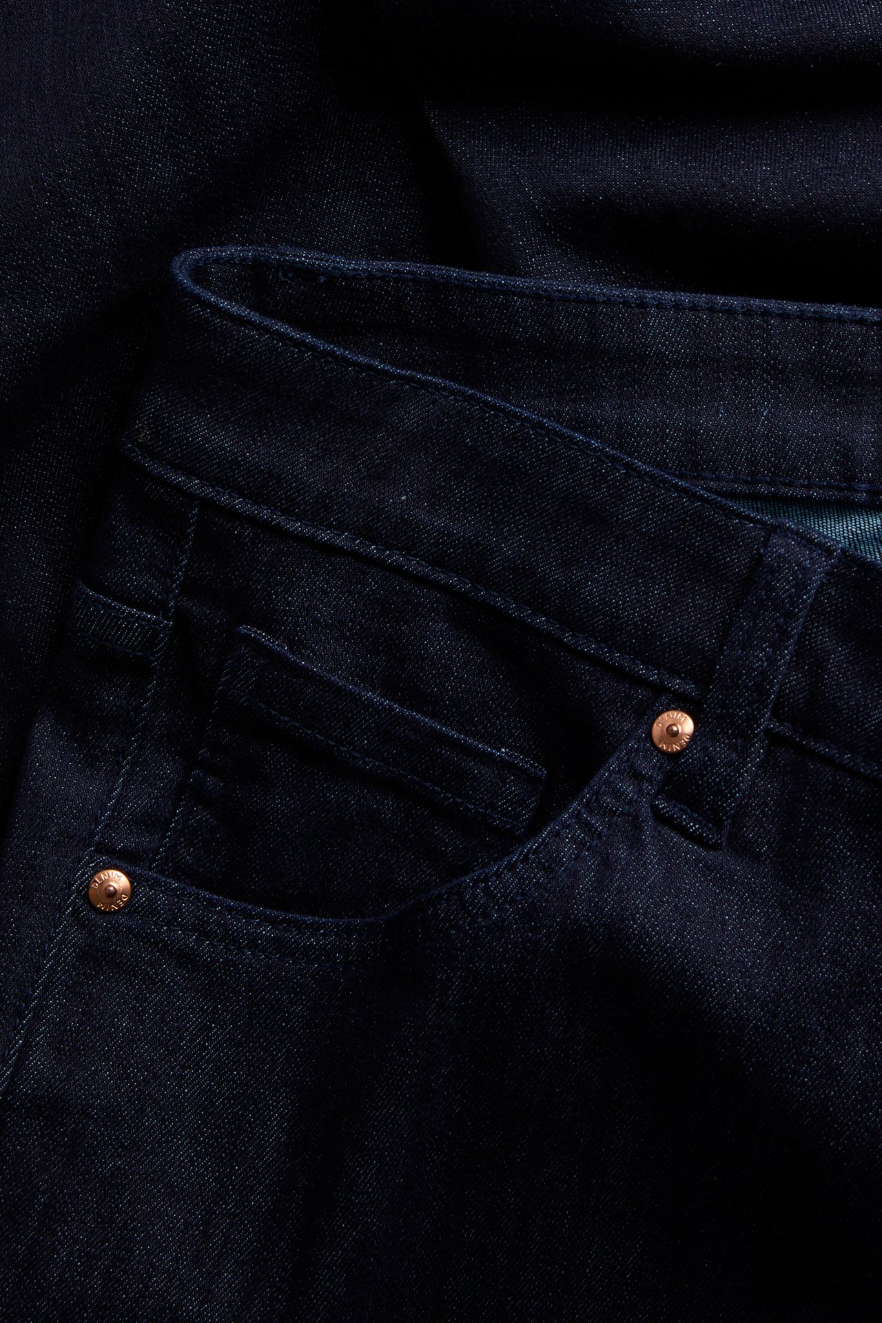 Närbild av mörkblå jeans med kopparnitar.