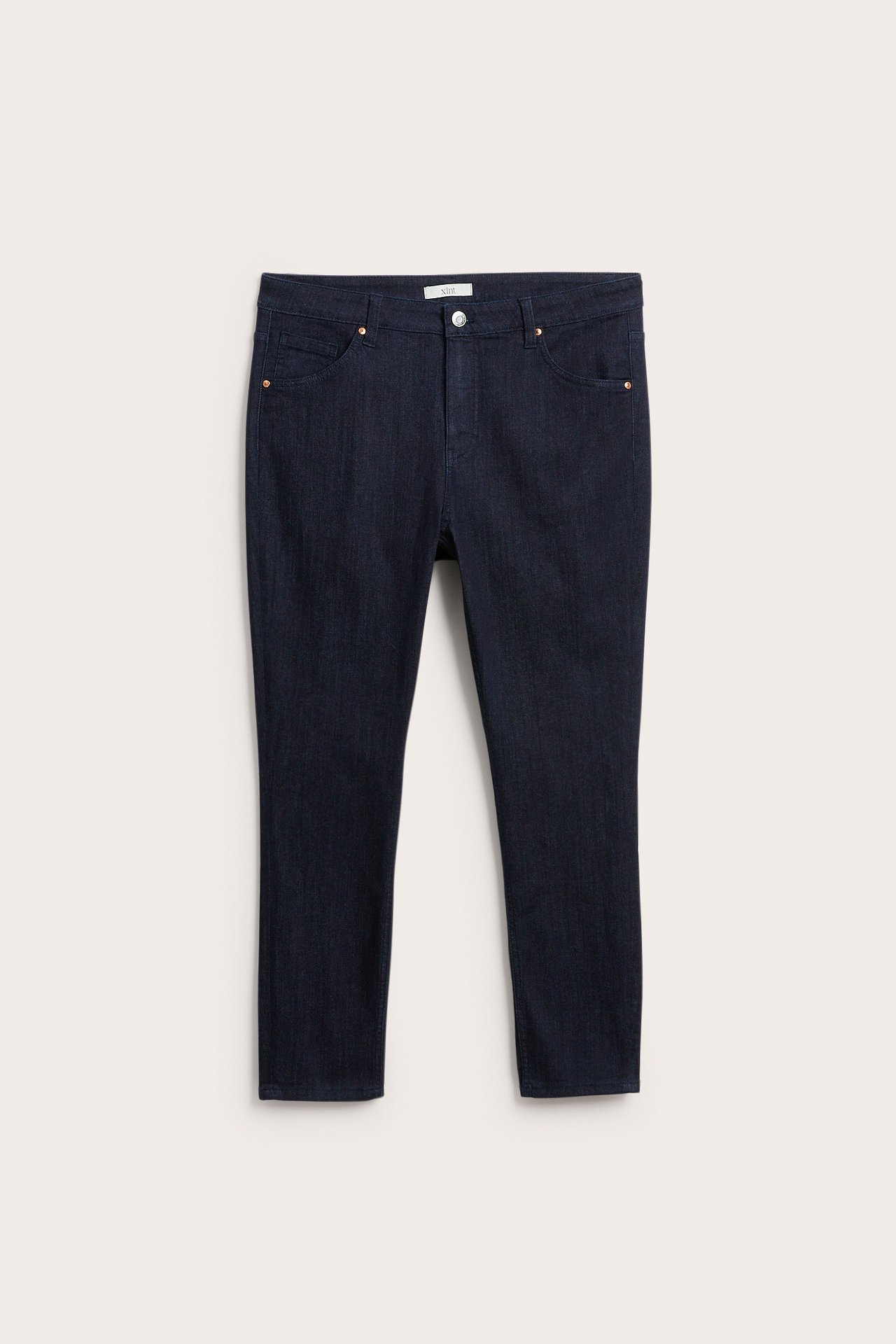 Framsida av mörkblå denim slim fit-jeans med knappgylf och kopparnitar.
