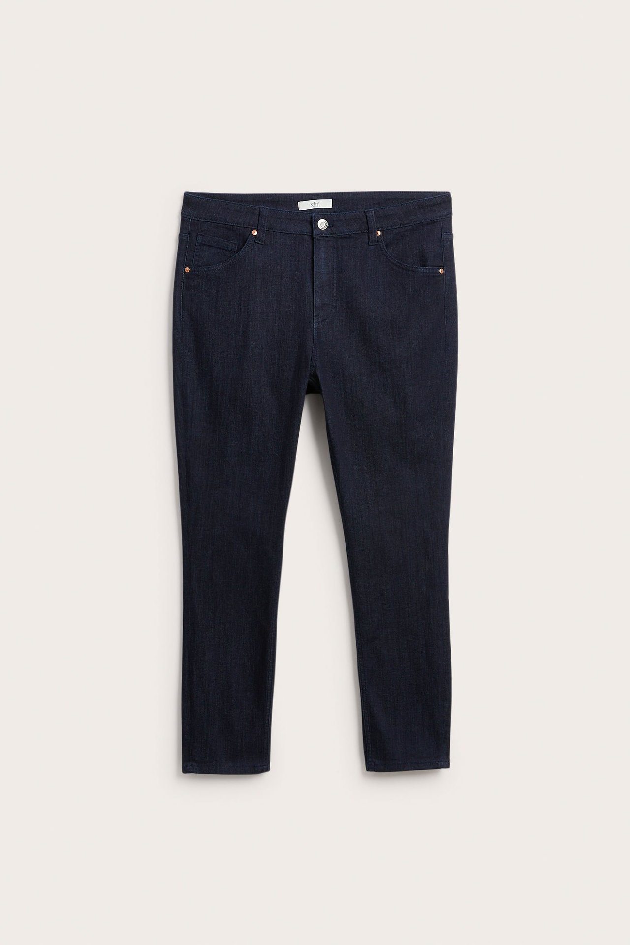 Framsida av mörkblå denim slim fit-jeans med knappgylf och kopparnitar.