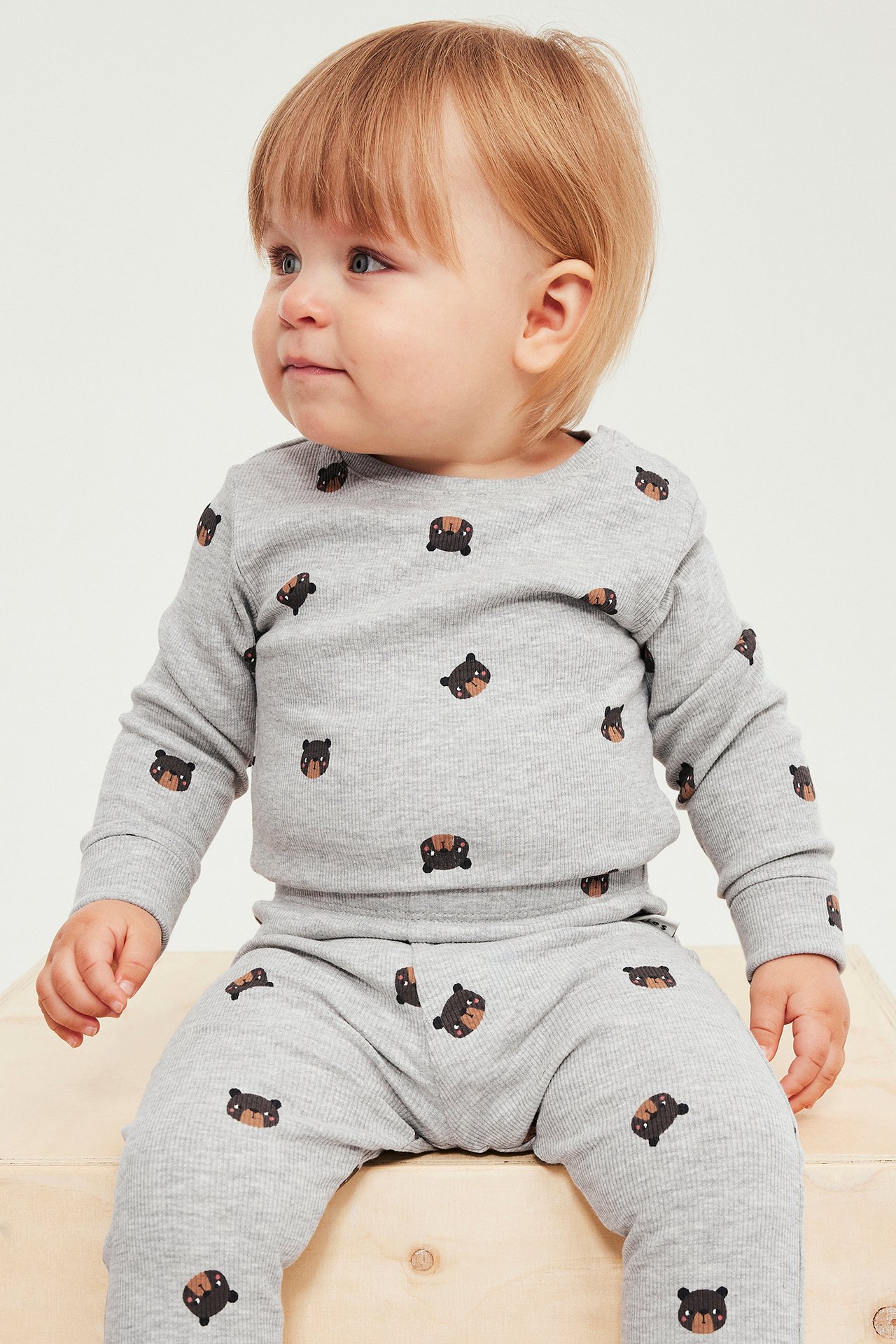 Edestä: Vauva yllään vaaleanharmaa ribbineulottu pyjamassetti kauttaaltaan karhukuviolla.