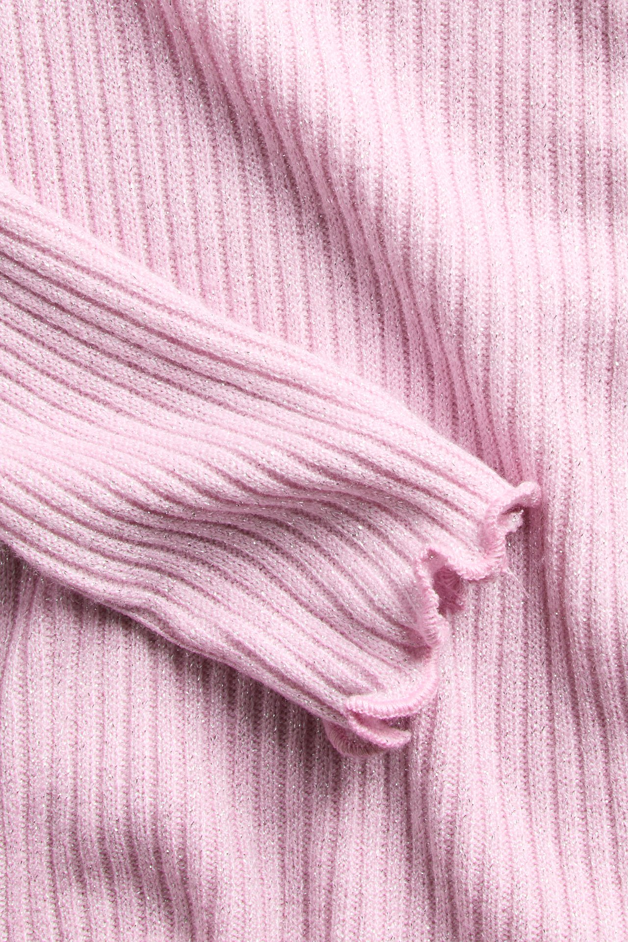 Närbild på rosa ribbstickad tröja med volangärmslut och skimrande detaljer.
