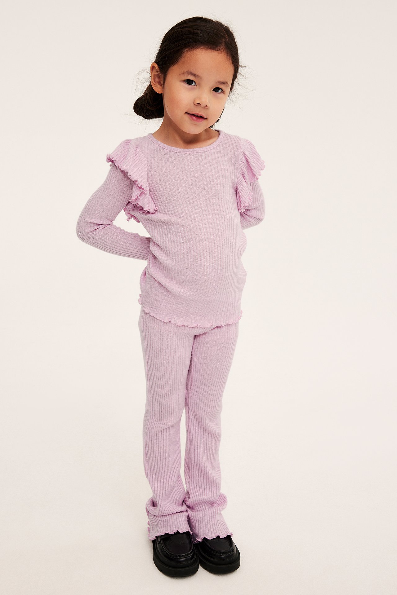 Framifrån, barn i lila ribbad volangtopp, matchande leggings och svarta skor.