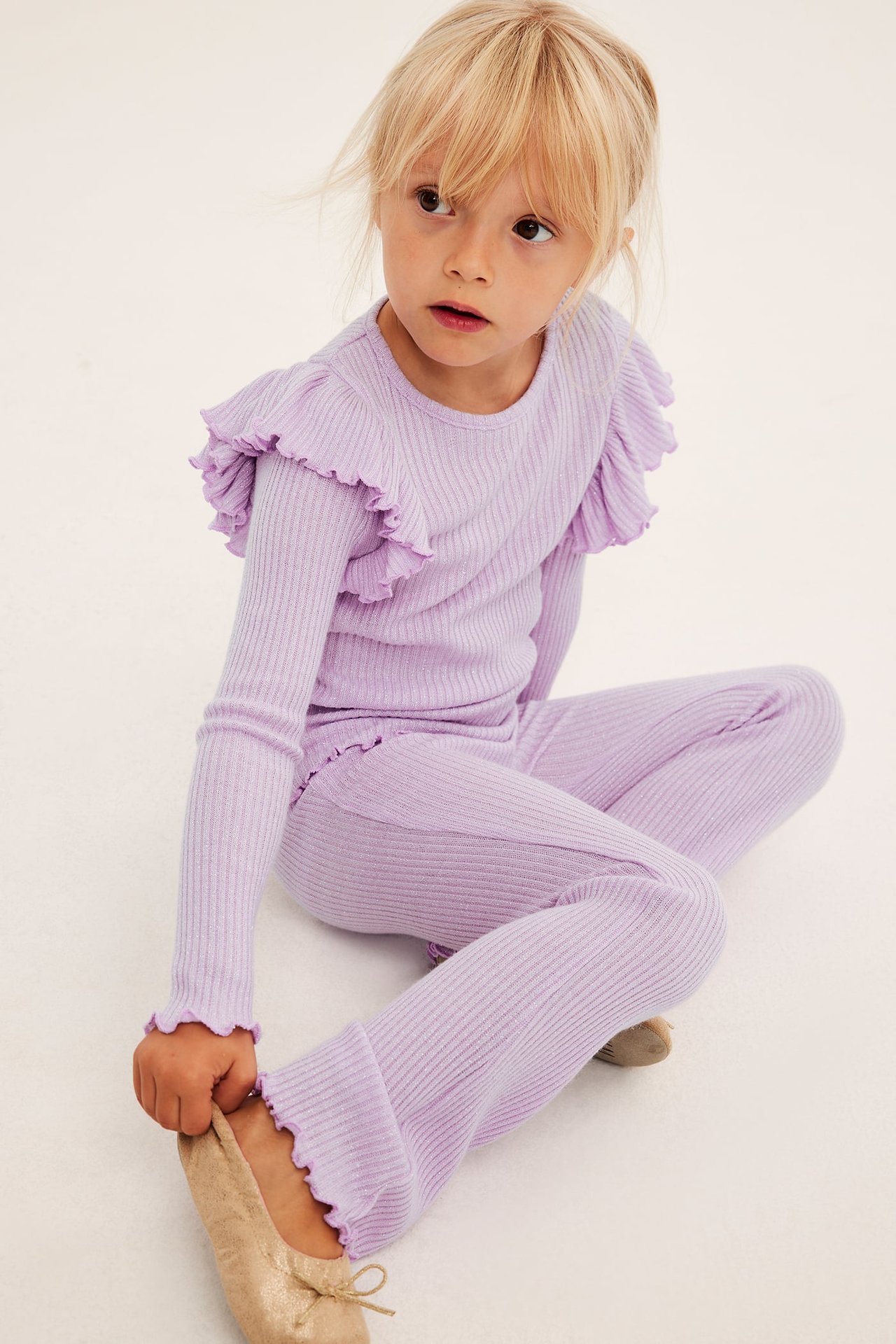 Barns lys lilla ribbestrikket topp med rysjeermer, matchende vide bukser og gullfargede ballerinasko.