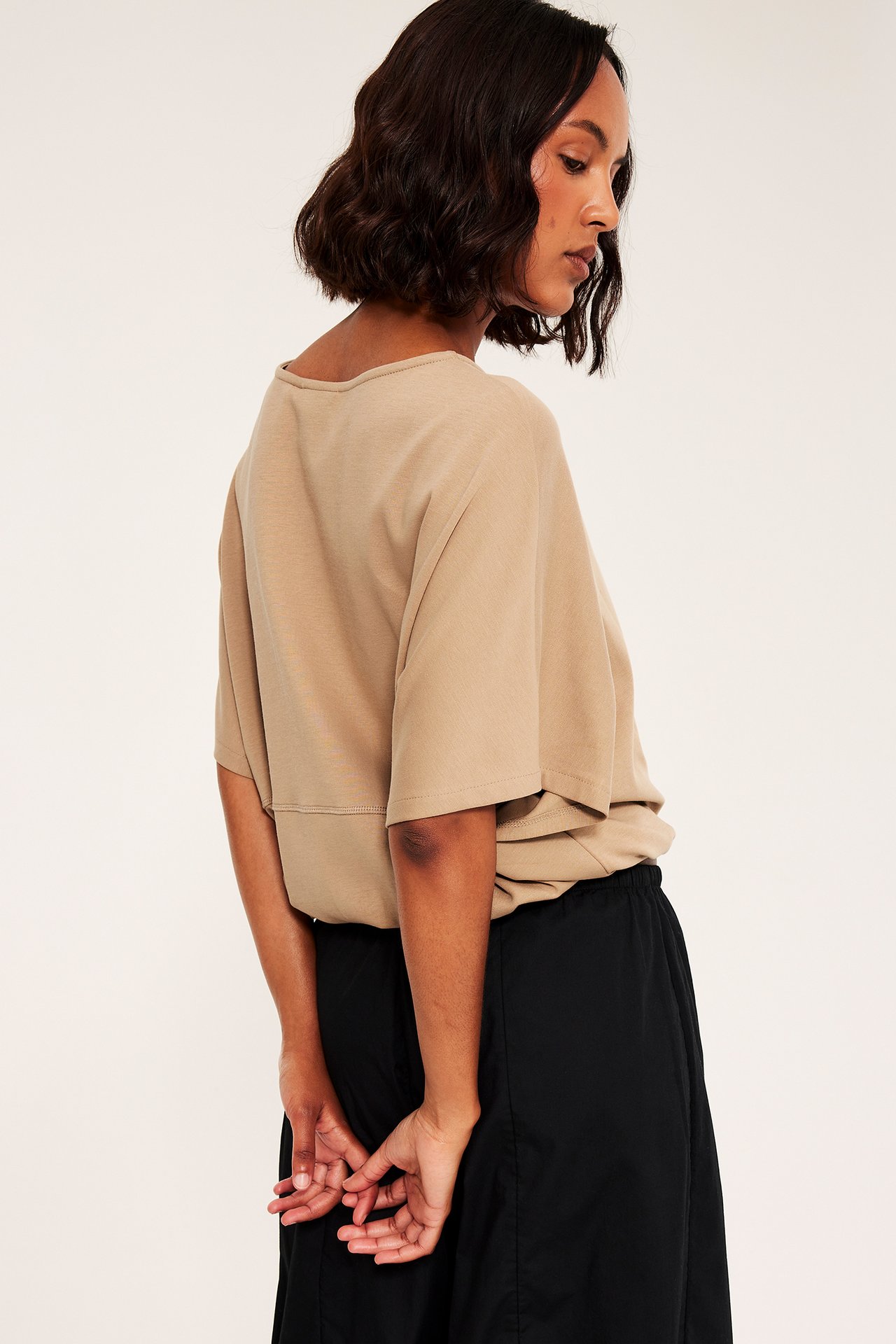 Bakifrån, kvinna i lös beige kortärmad topp och svarta byxor.