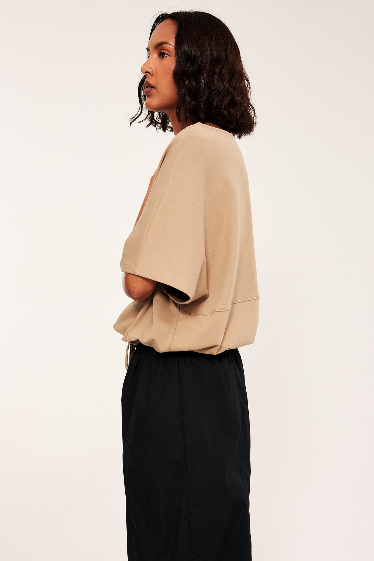 Sidorbild av kvinna i beige oversized kortärmad topp och svart midikjol med dragsko i midjan.