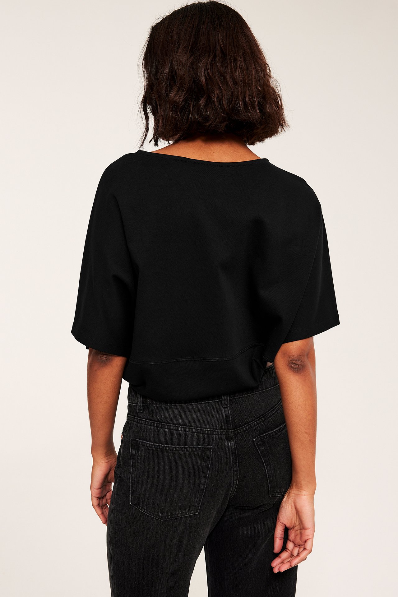 Kvinna sedd bakifrån i svart kortärmad croppad topp och mörkgrå jeans.