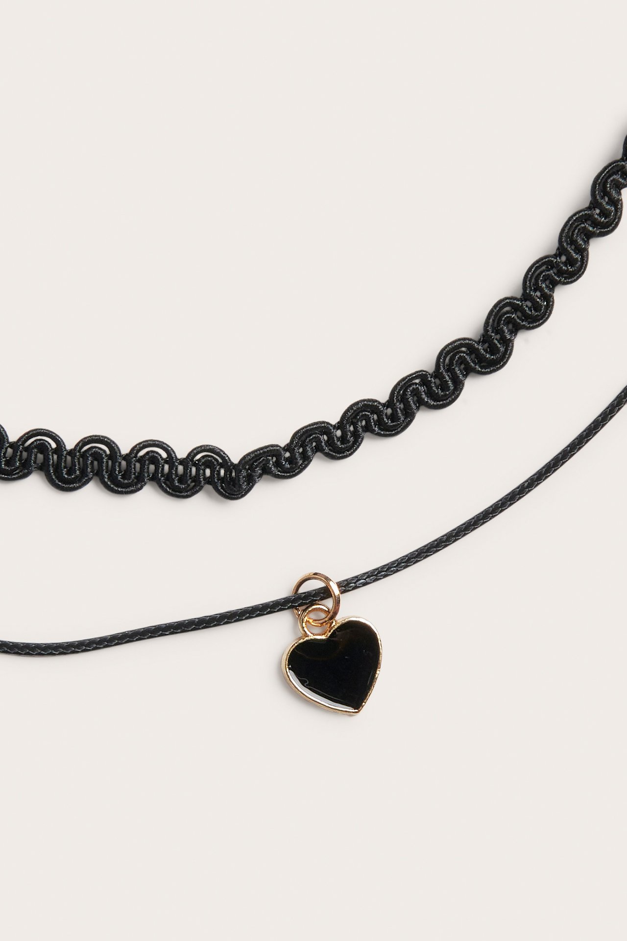 Närbild på ett svart dubbelhalsband med mönstrad choker och ett svart hjärthänge med guldkant.
