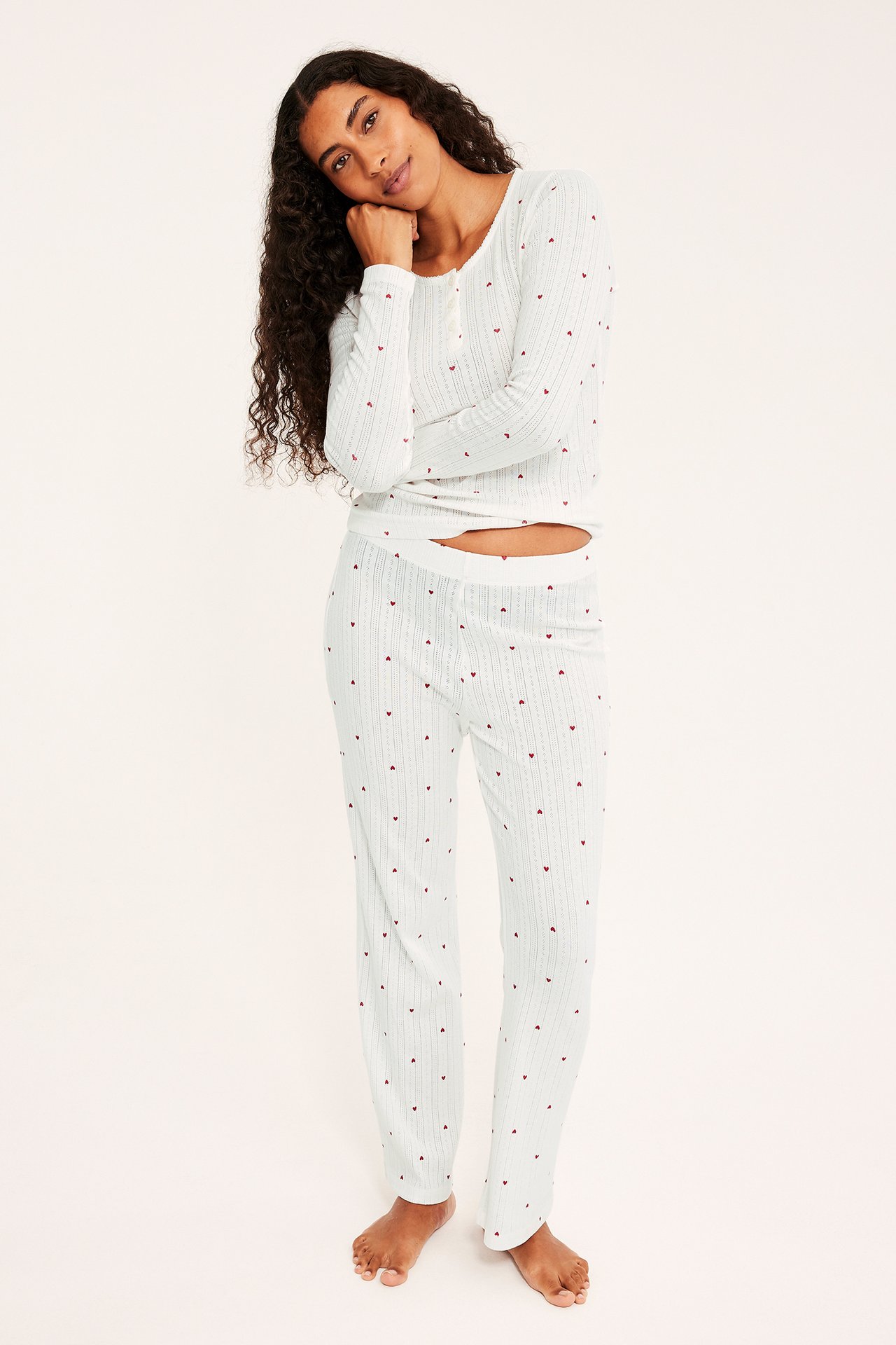 Etunäkymä naisesta yllään valkoinen ribbipyjama punaisella sydänkuviolla.