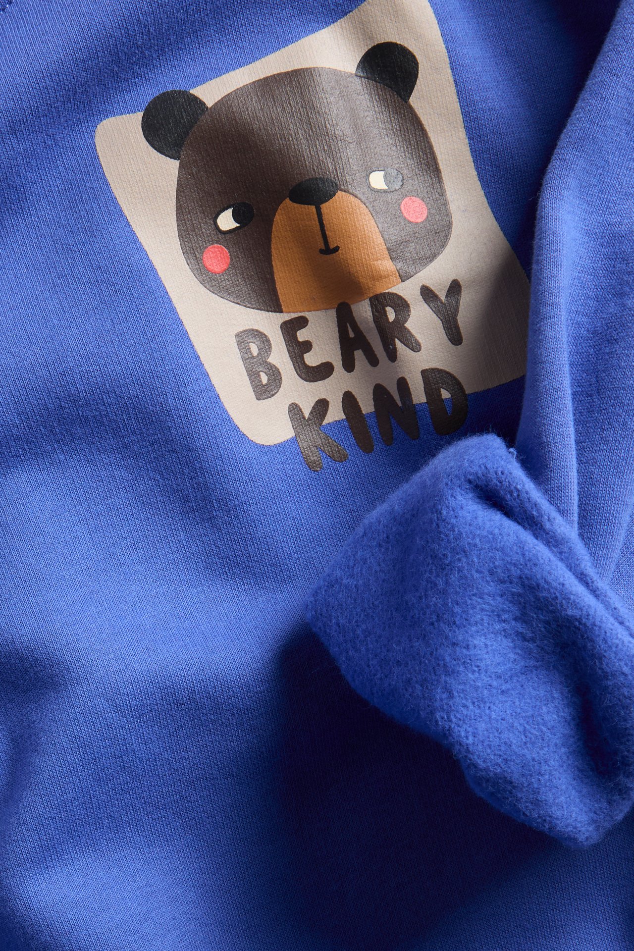 Lähikuva sinisestä lasten paidasta, jossa ruskea karhupainatus ja teksti "BEARY KIND".