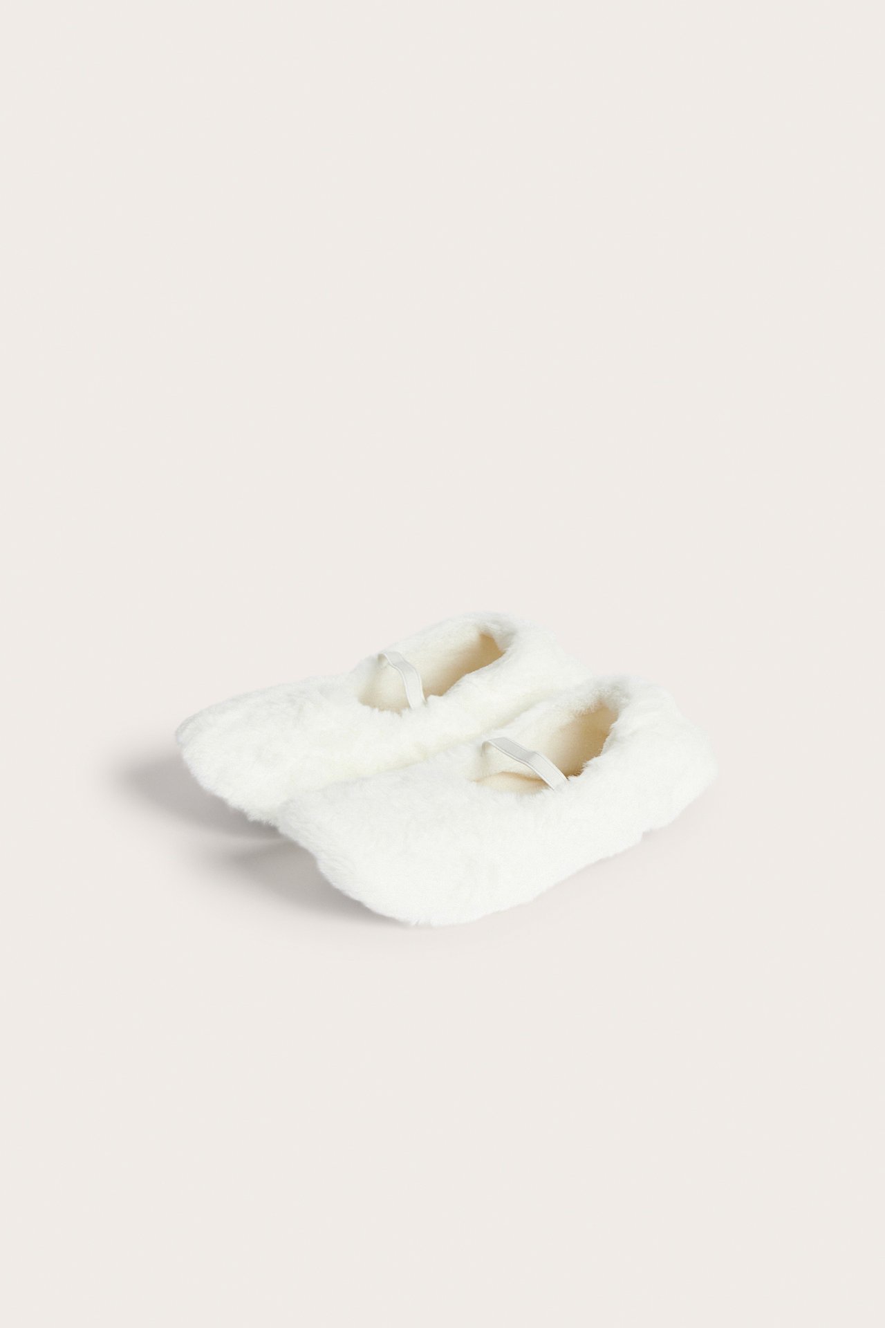 Vinklad vy av ett par vita fluffiga tofflor med smala remmar.
