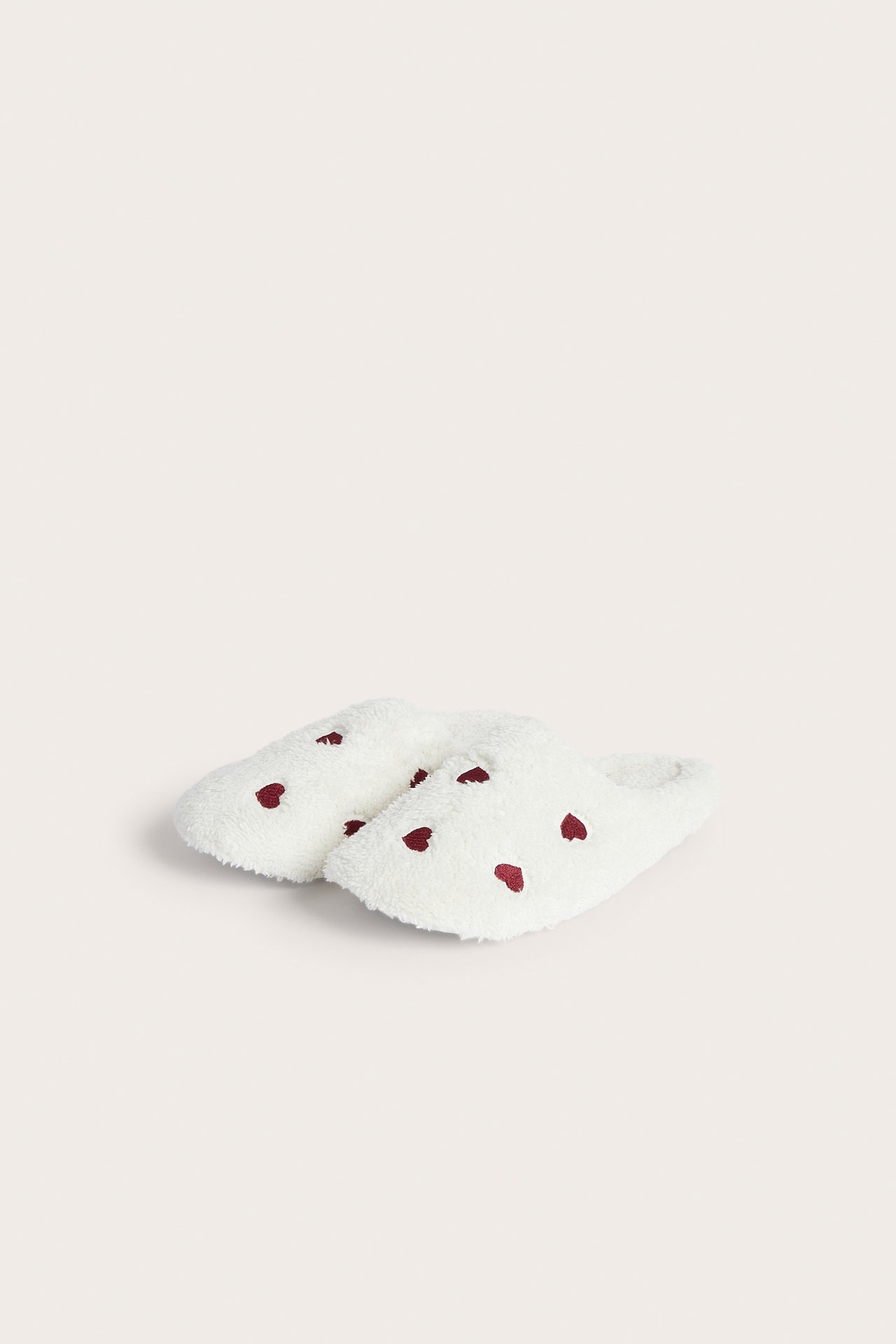 Hög vinkelvy av ett par vita fluffiga tofflor med röda hjärtan.