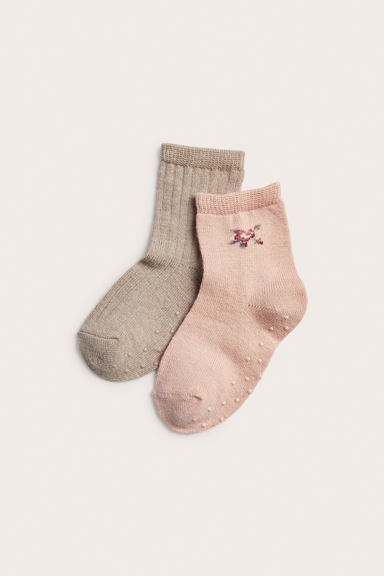 Uppifrån: rosa babysocka med blommig brodyr och beige ribbad, båda med greppsula.