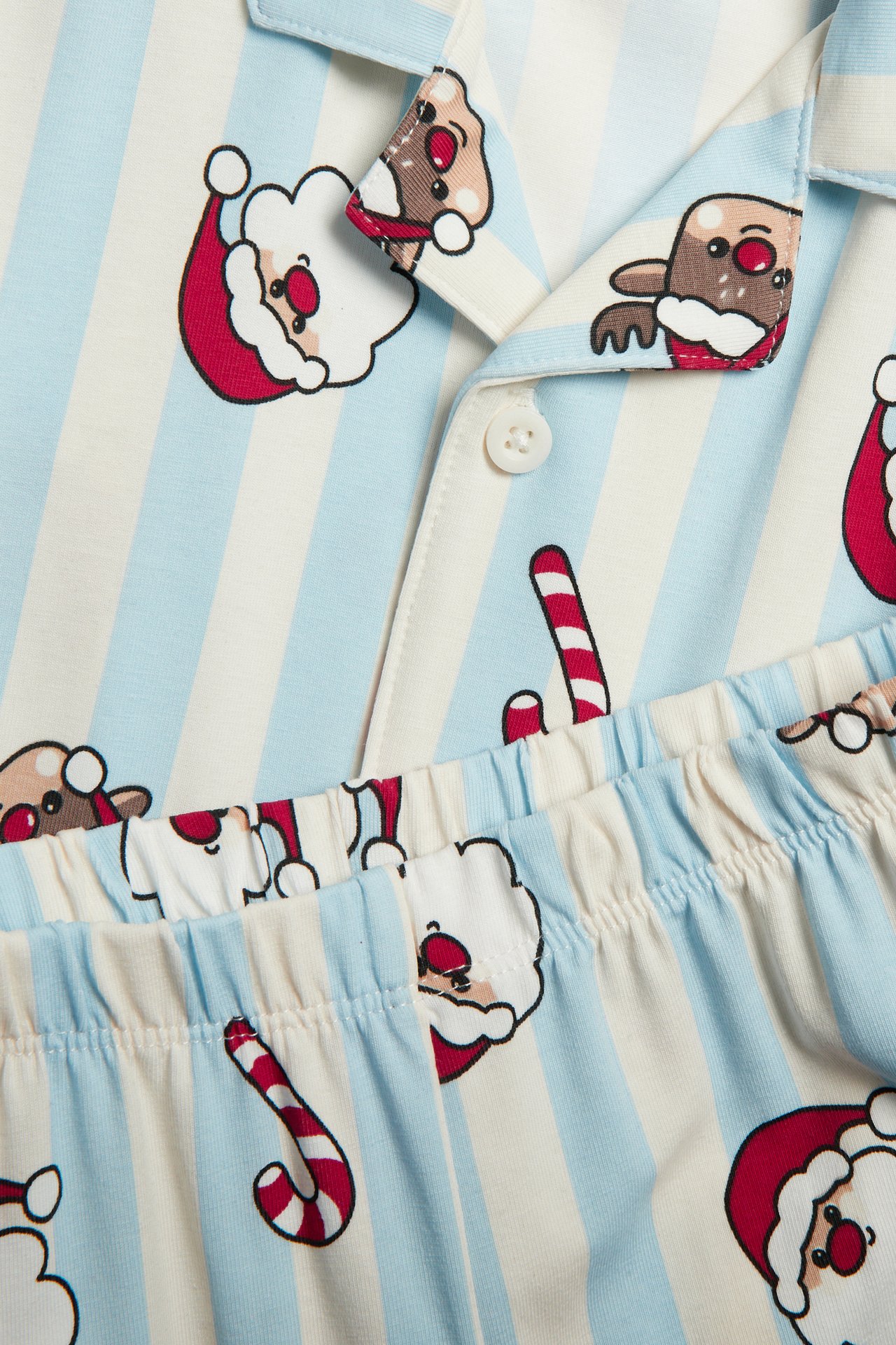 Närbild av ett pyjamasset med ljusblå och vita ränder, mönstrad med tomte, renar och polkagrisar.