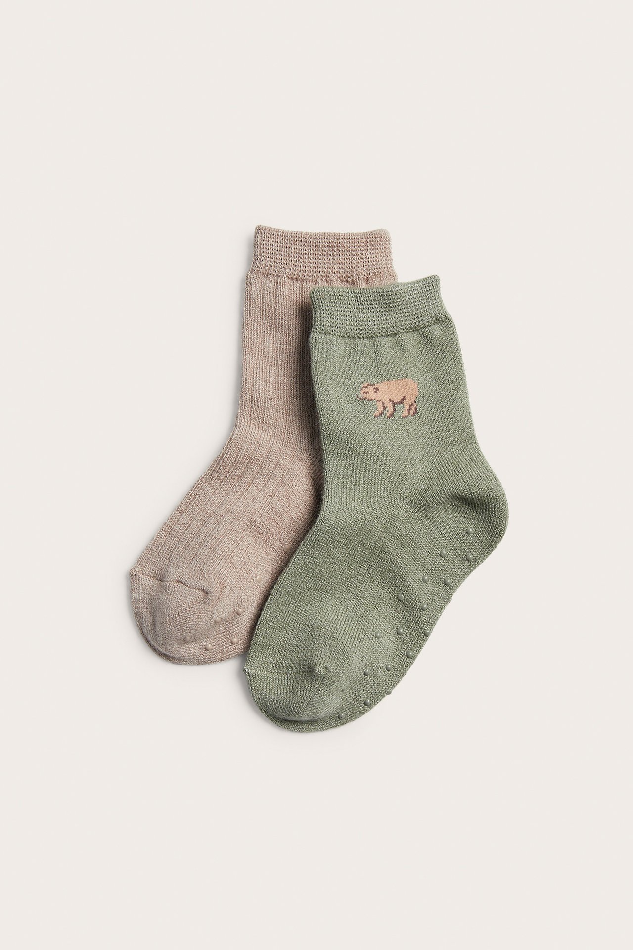 Två par halkfria babysockor: en salviagrön med djurbroderi, en ljusbrun.