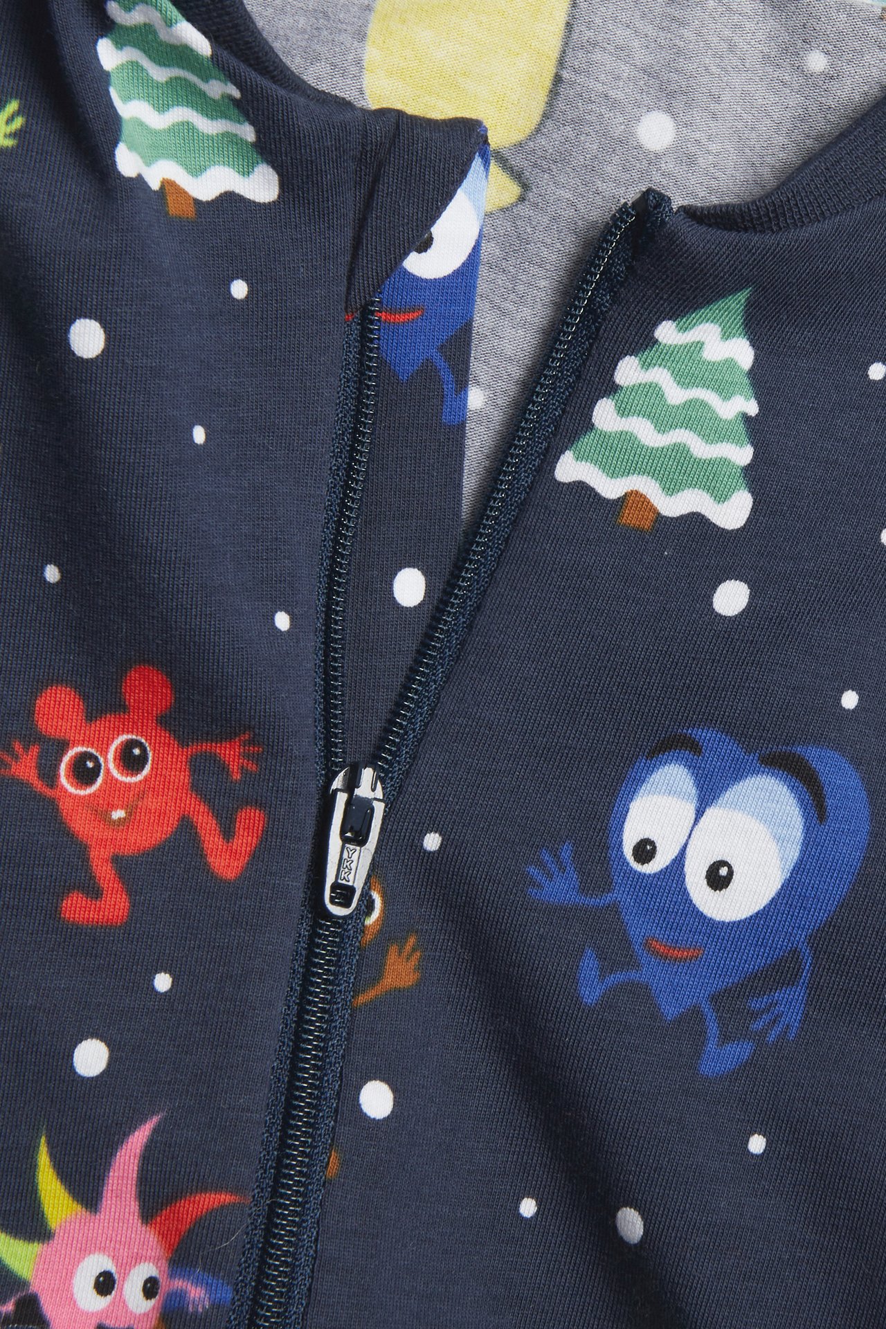 Närbild av mörkblå babydräkt med färgglatt jultryck och delvis öppen marinblå dragkedja.