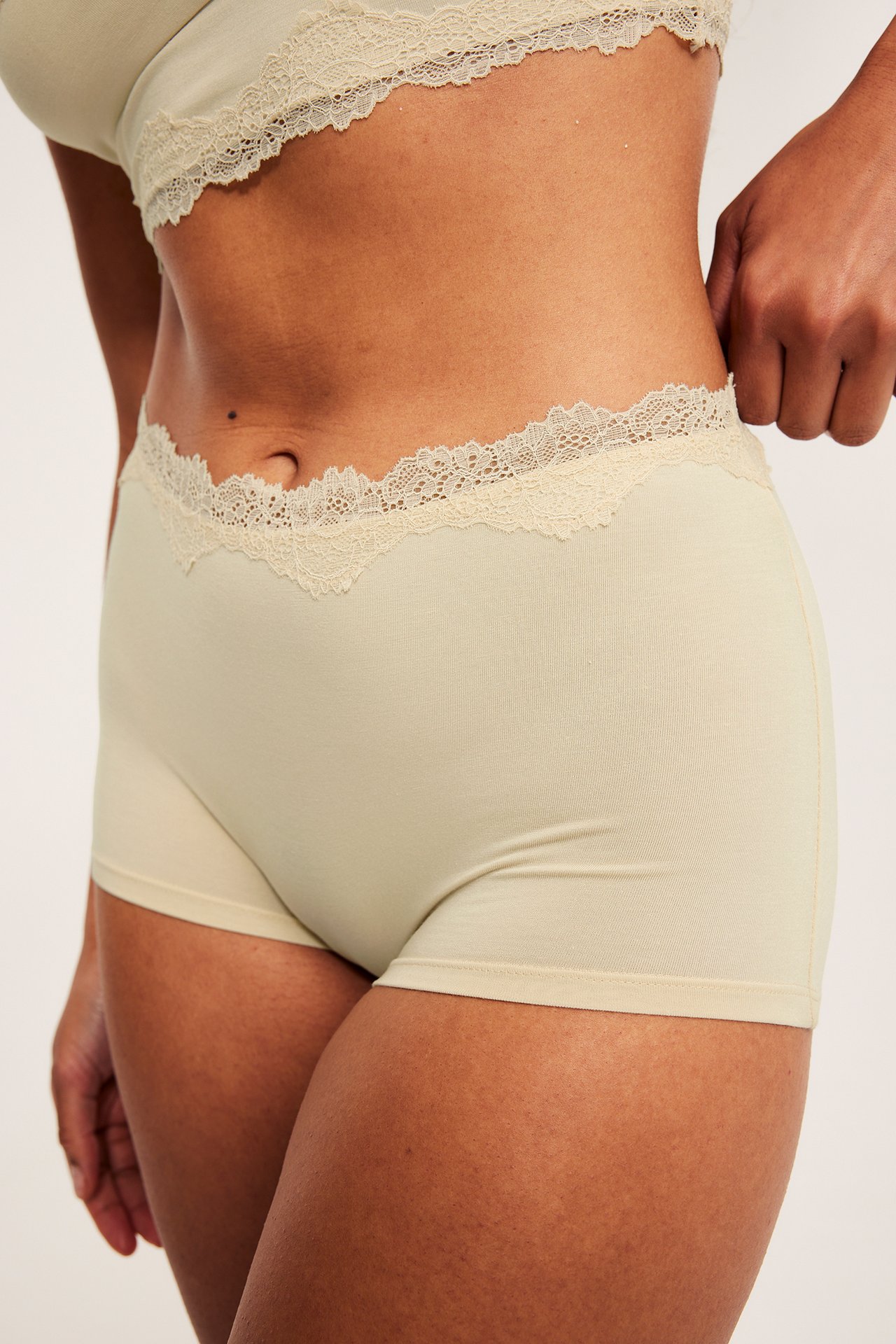Snett framifrån: kvinna i beiga modal-boxertrosor med spetskant och matchande behå.