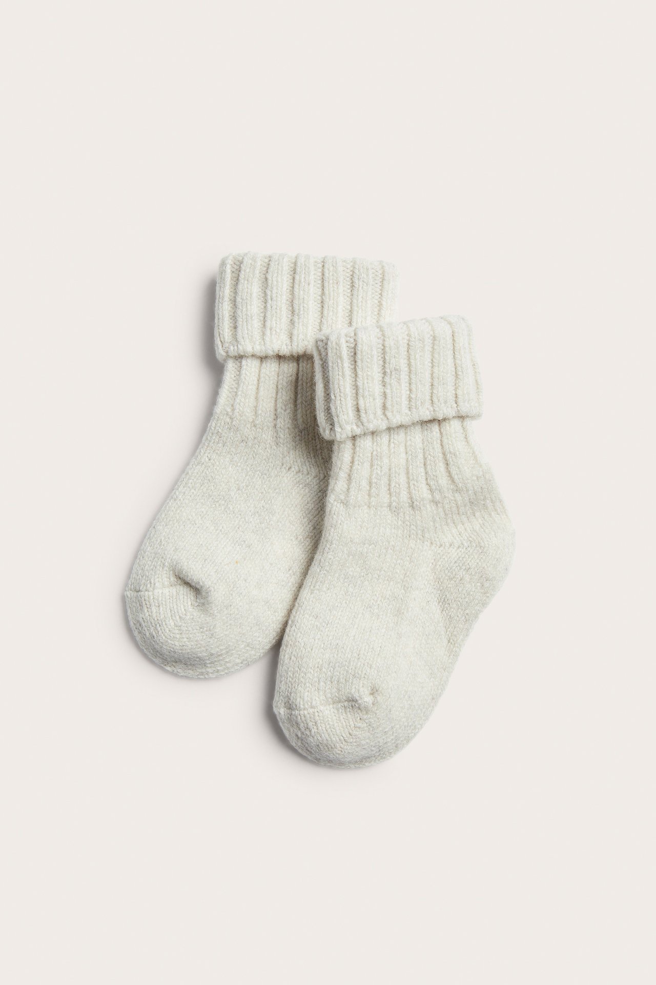 Ljusbeige stickade babysockor med ribbstickade muddar, toppvy.