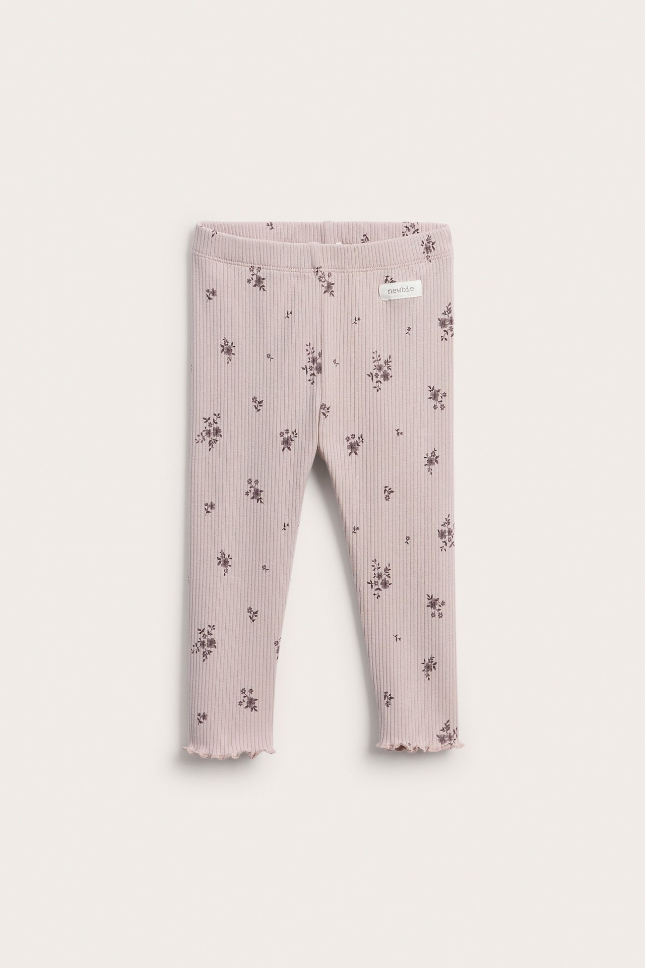 Frontbilde av ribbestrikkede baby-leggings i lys rosa med mørkt blomstertrykk og kruskant.
