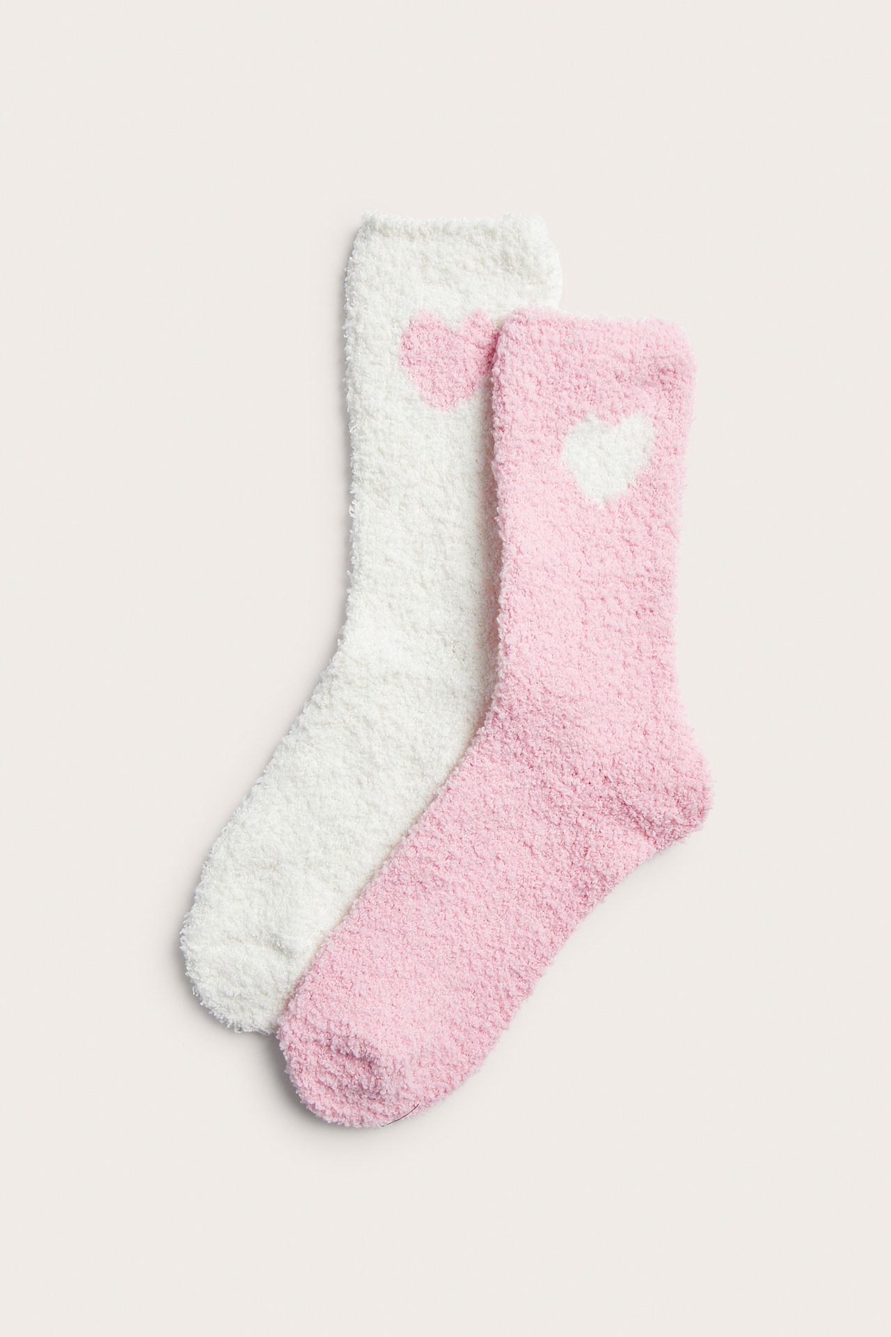 Framifrån: två fluffiga strumpor, en rosa med vitt hjärta och en vit med rosa hjärta.