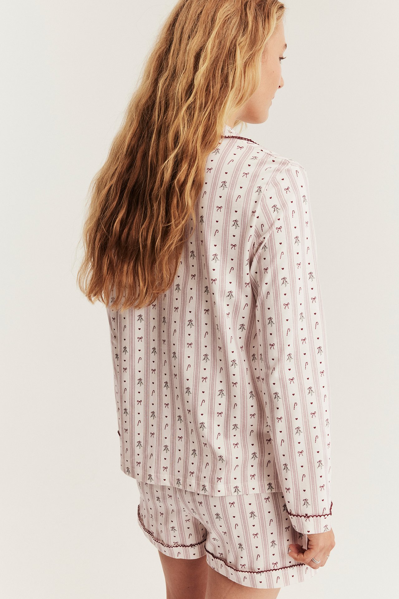 Baksida av kvinna i vit och vinrödrandig pyjamas med polkagris- och rosettmönster.