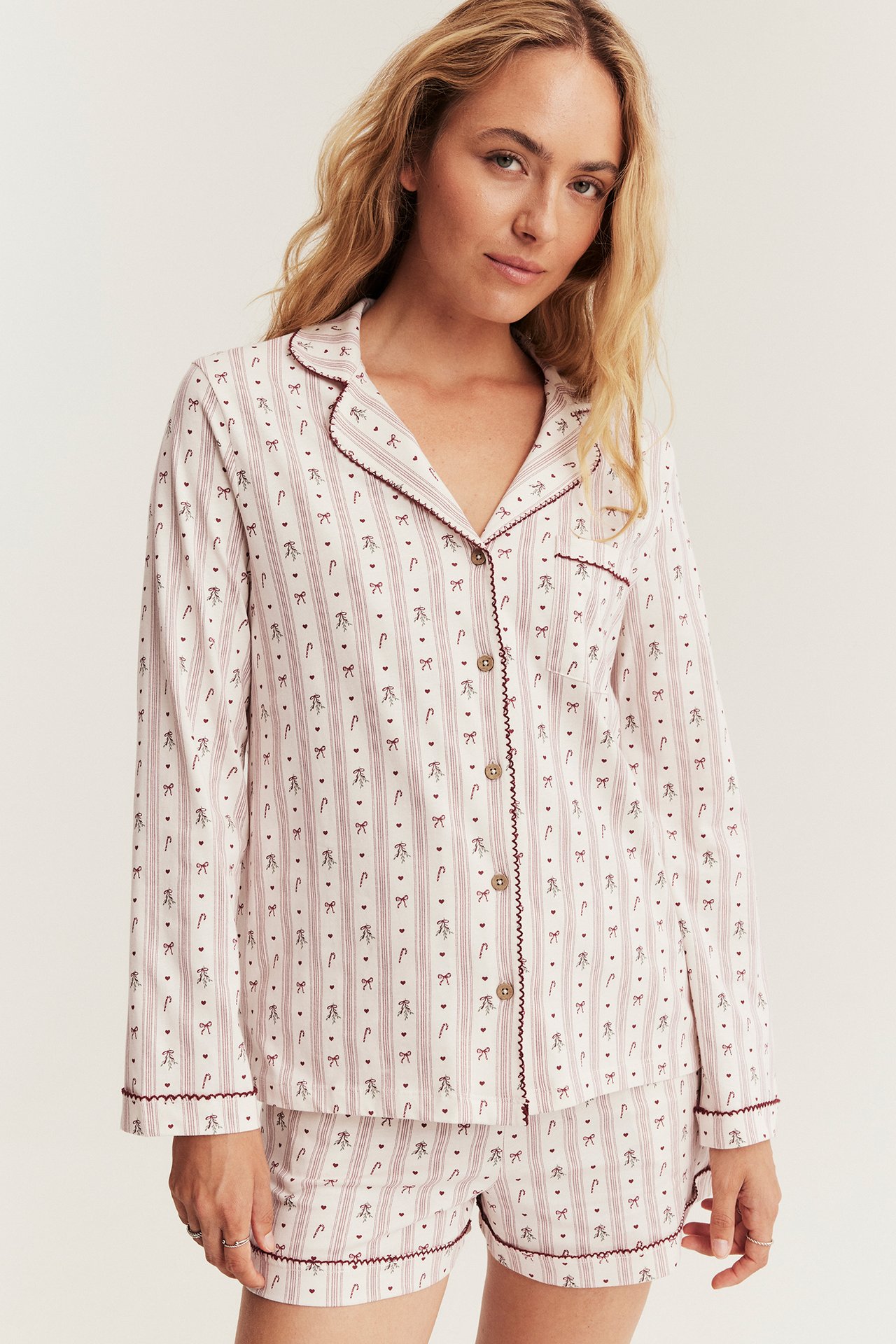 Kvinne i stripet pyjamas med sukkerstenger, sløyfer, rød kamskjellkant, topp og shorts.