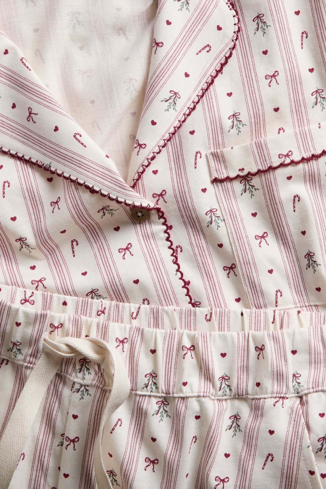 Närbild av randig pyjamas i gräddvitt och rött med tryck av hjärtan, rosetter, polkagrisar och mistel.