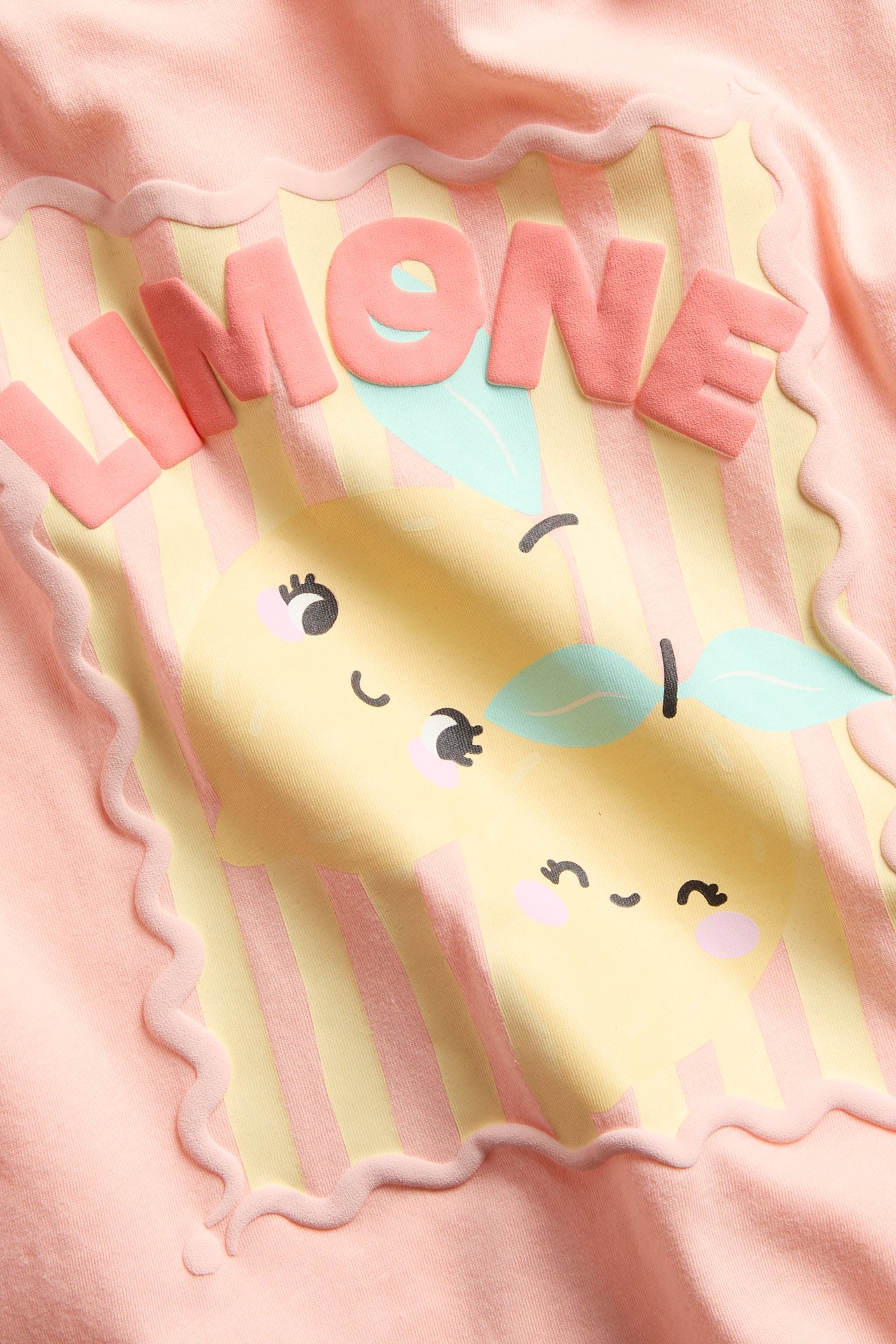 Lähikuva edestä korallinvärisestä puuvillaisesta T-paidasta, jossa keltainen sitruuna ja 'LIMONE'-painatus.