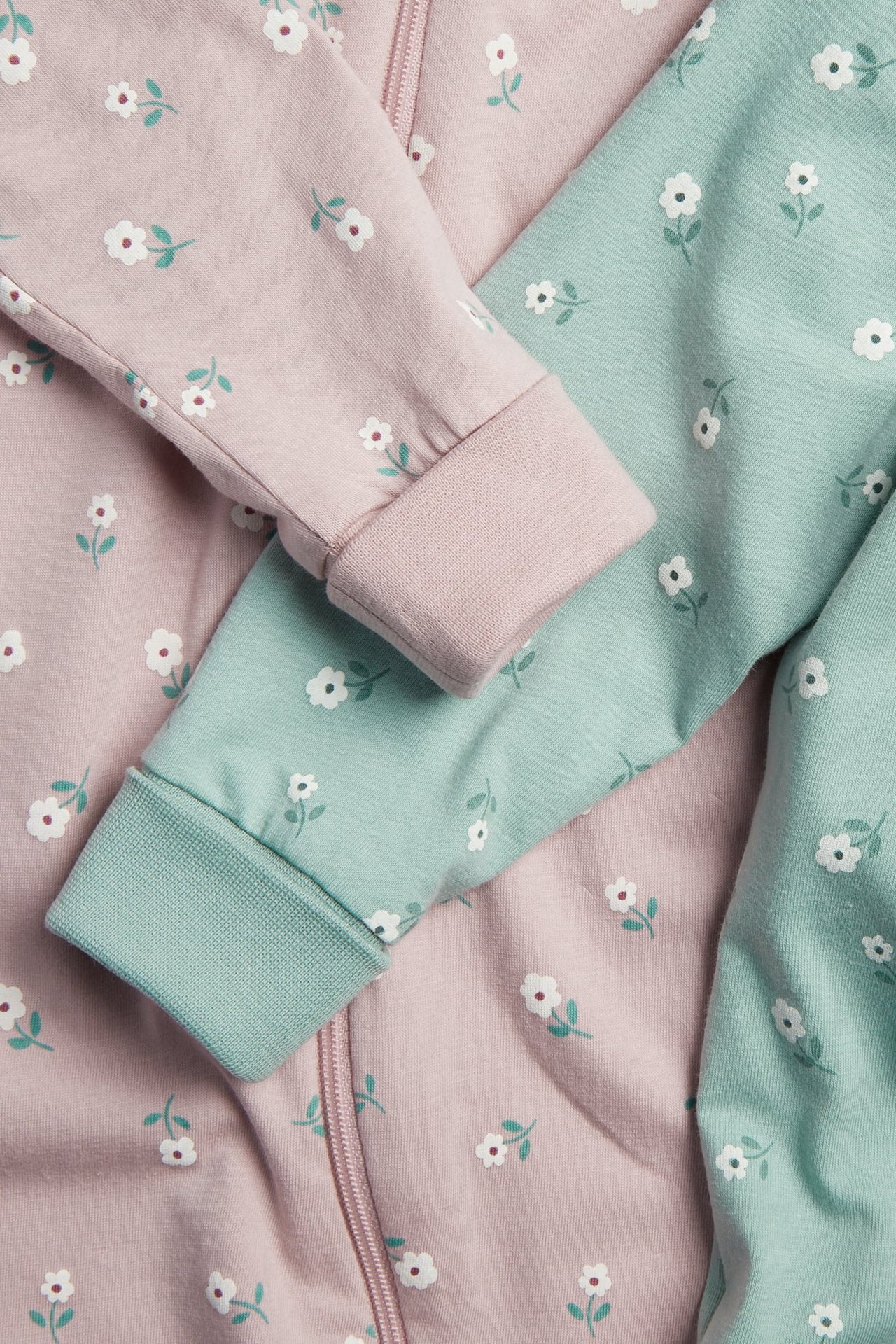Närbild på en rosa blommig babyoverall med dragkedja och en mintgrön blommig babyoverall.
