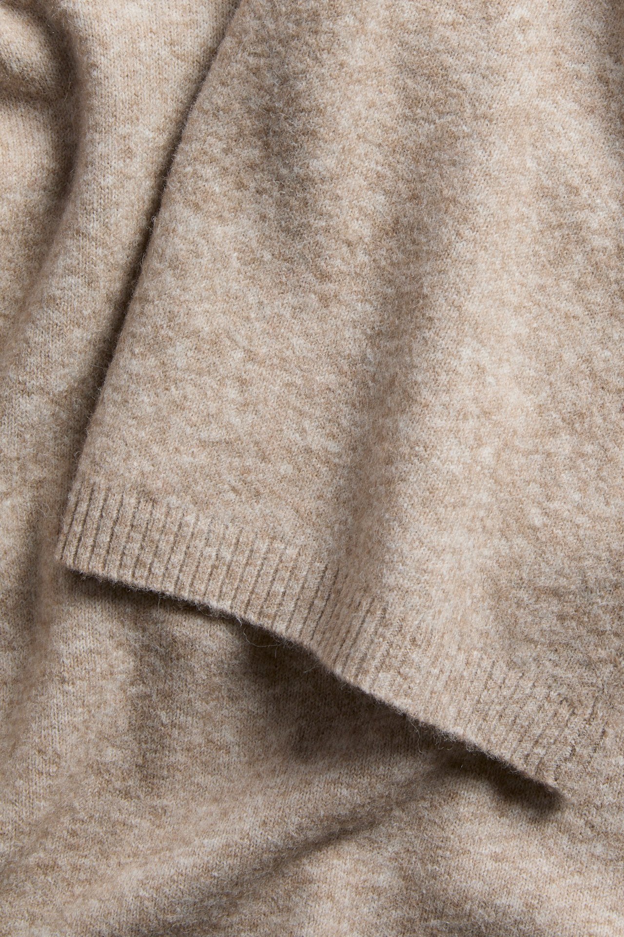 Närbild av ett ljusbeige stickat plagg med ribbad kant.