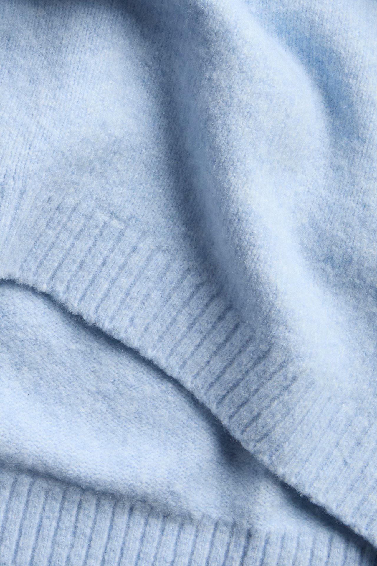 Lähikuva vaaleansinisestä pehmeästä neulepuserosta, jossa on ribbineulottuja yksityiskohtia.