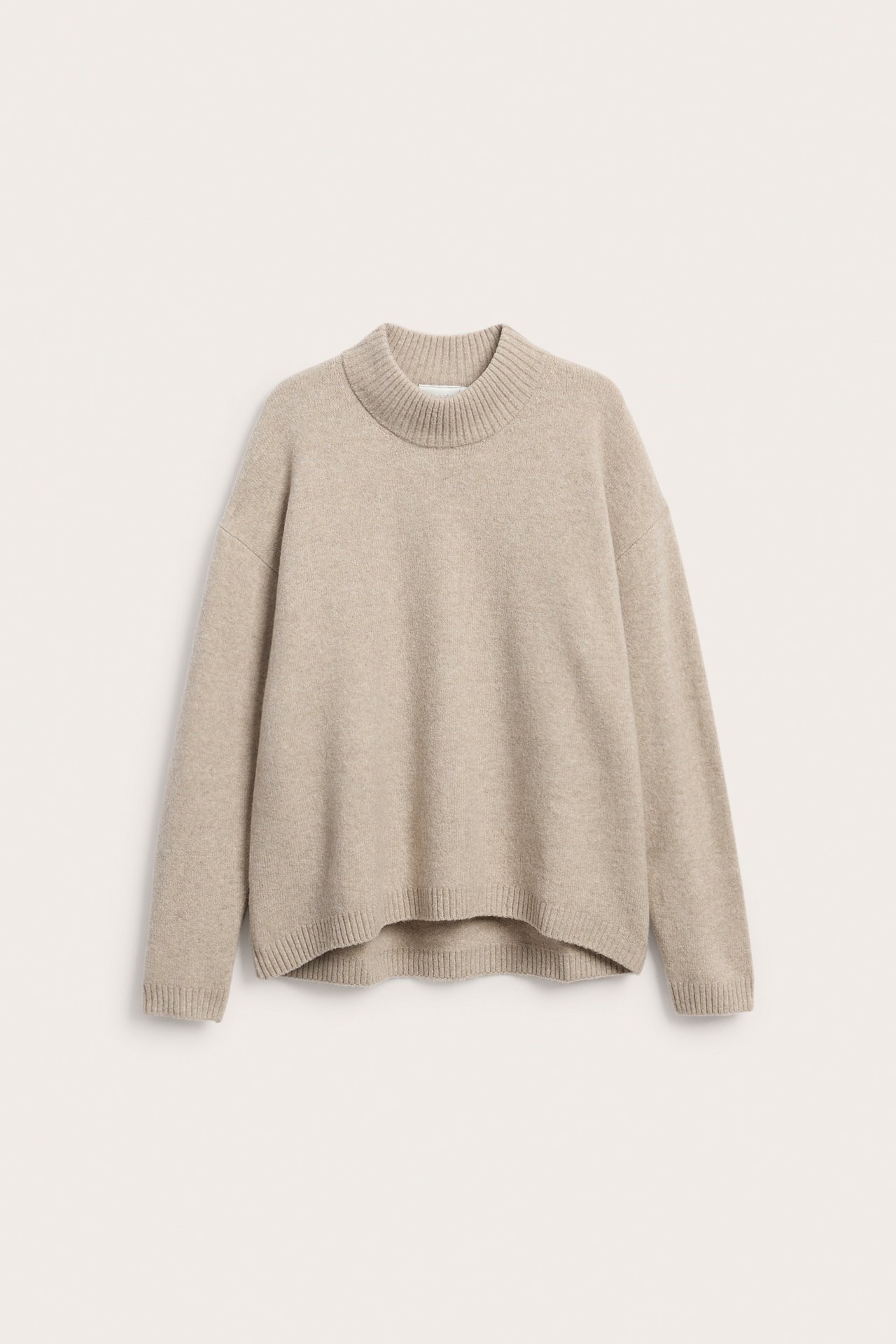 Edestä päin rento beige neulepaita, jossa on pystykaulus ja ribbineulottuja yksityiskohtia.