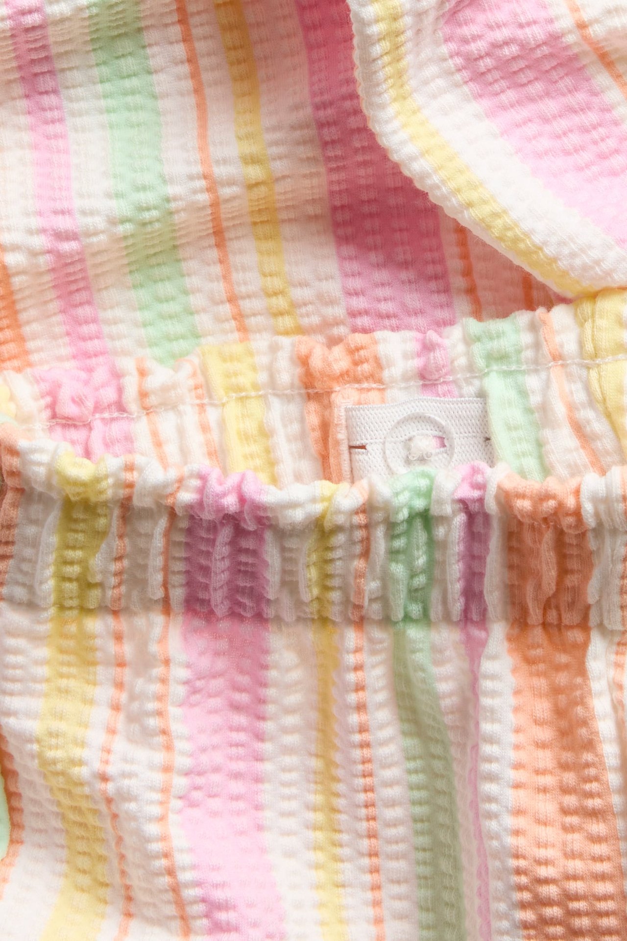 Lähikuva lasten luonnonvalkoisista raidallisista seersucker-culottes-housuista joustovyötäröllä ja napilla.