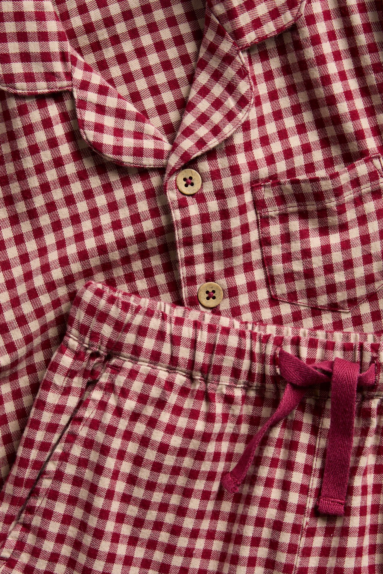 Närbild på röd och benvit rutig flanellpyjamas med träknappar och dragsko.