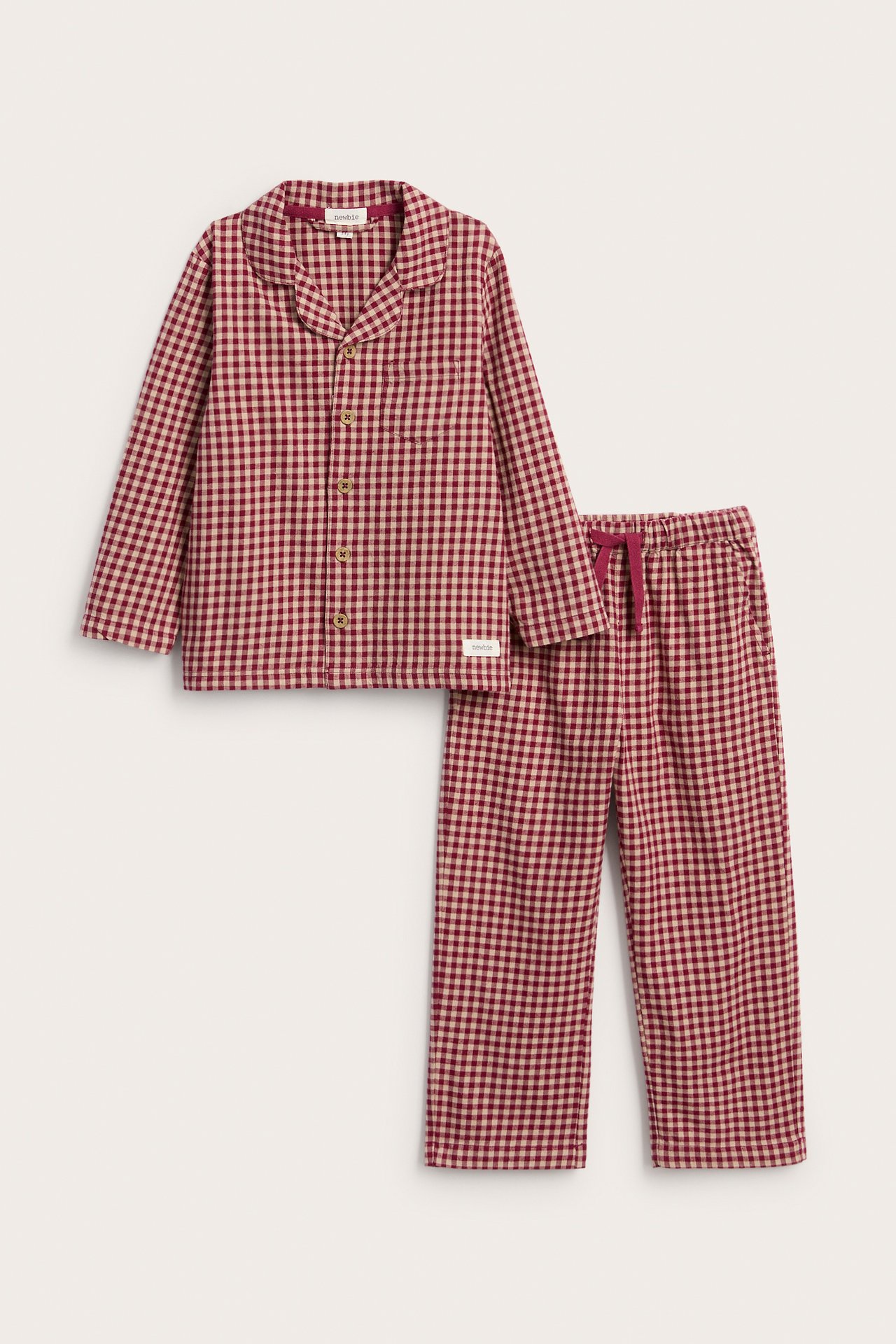 Framsida av barns röda och beiga ginghamrutiga pyjamasset: knäppt tröja, dragskobyxor.