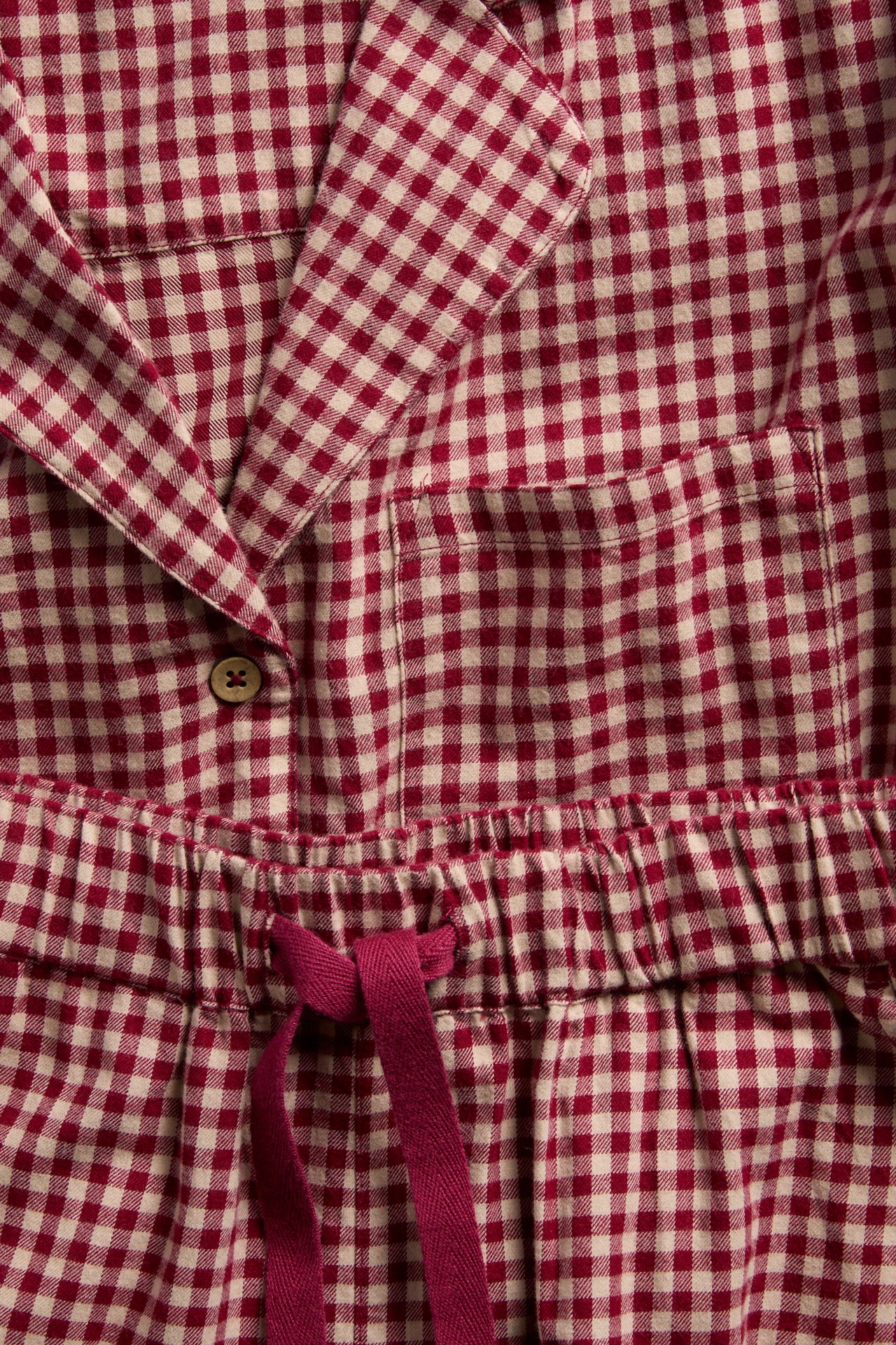 Lähikuva: Punakerma ruudullinen pyjamassetti kauluksella, napilla, rintataskulla ja kiristysnyörillä.