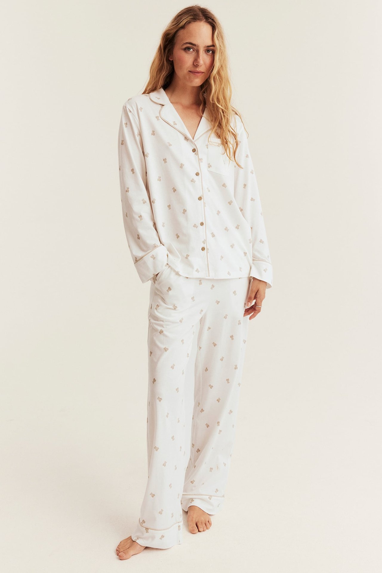 Edestäpäin: nainen valkoisessa pitkähihaisessa pyjama-setissä ruskealla karhukuvioinnilla.