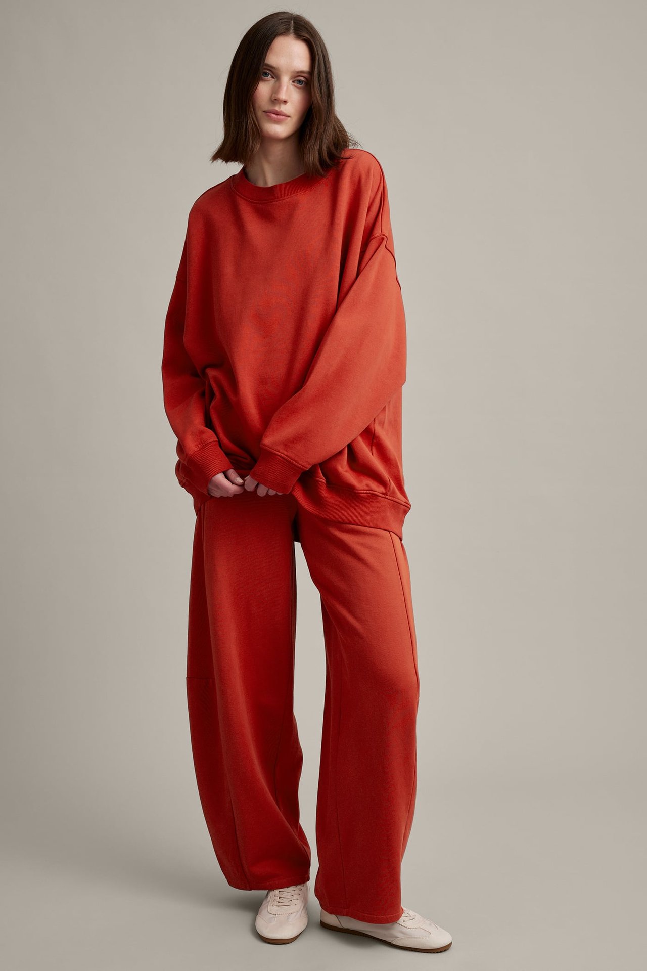 Forfra: kvinne i en oversize oransjerød sweatshirt med matchende vide bukser og lyse joggesko.