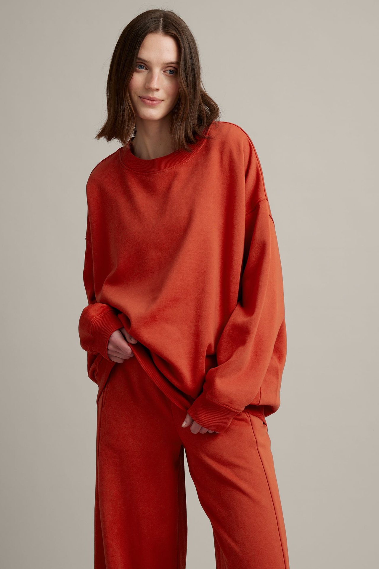 Frontbilde av kvinne i en oversized rustoransje crew-neck genser og matchende vide joggebukser.