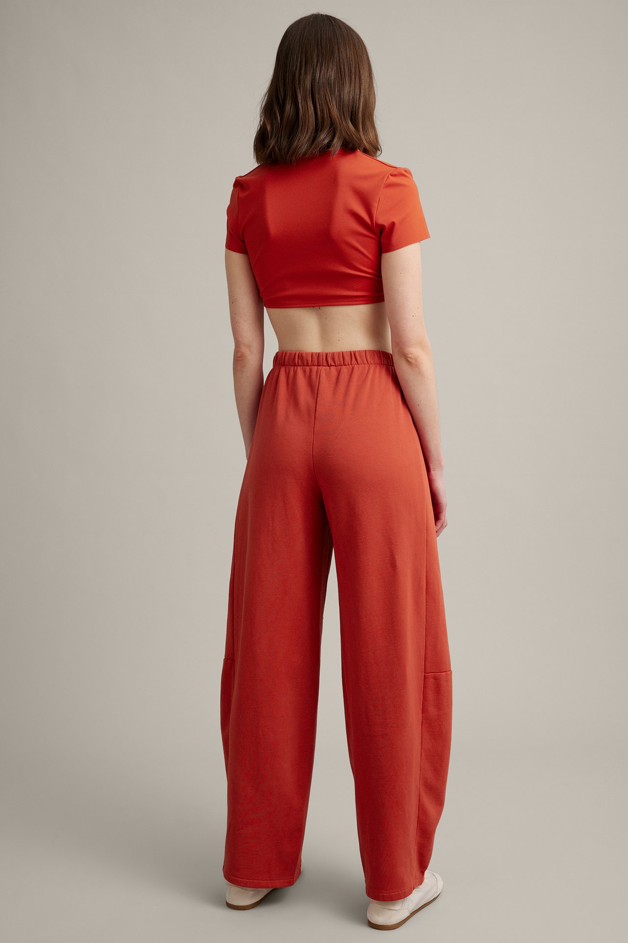 Widok z tyłu: kobieta w rdzawych, szerokich spodniach dresowych i pasującym krótkim topie.