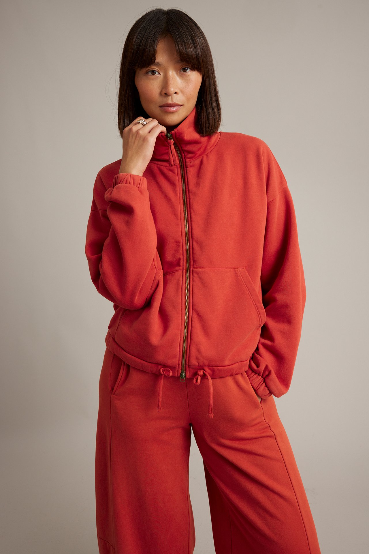 Framifrån: kvinna i bränd orange tröja med dragkedja och matchande vida sweatpants.