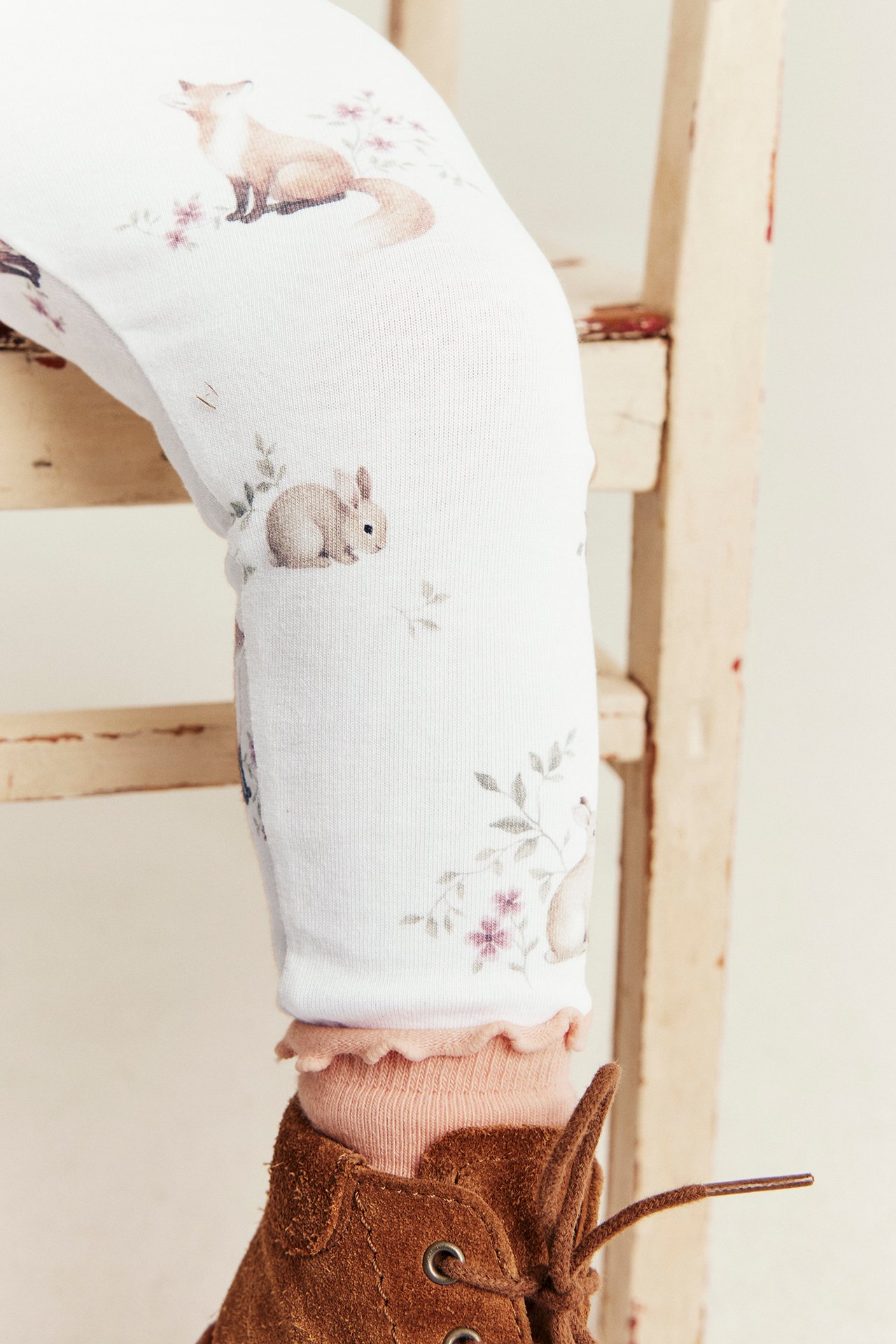 Nærbilde av et barns ben iført hvite mønstrede leggings, rosa sokker og brune semskede snørestøvler.